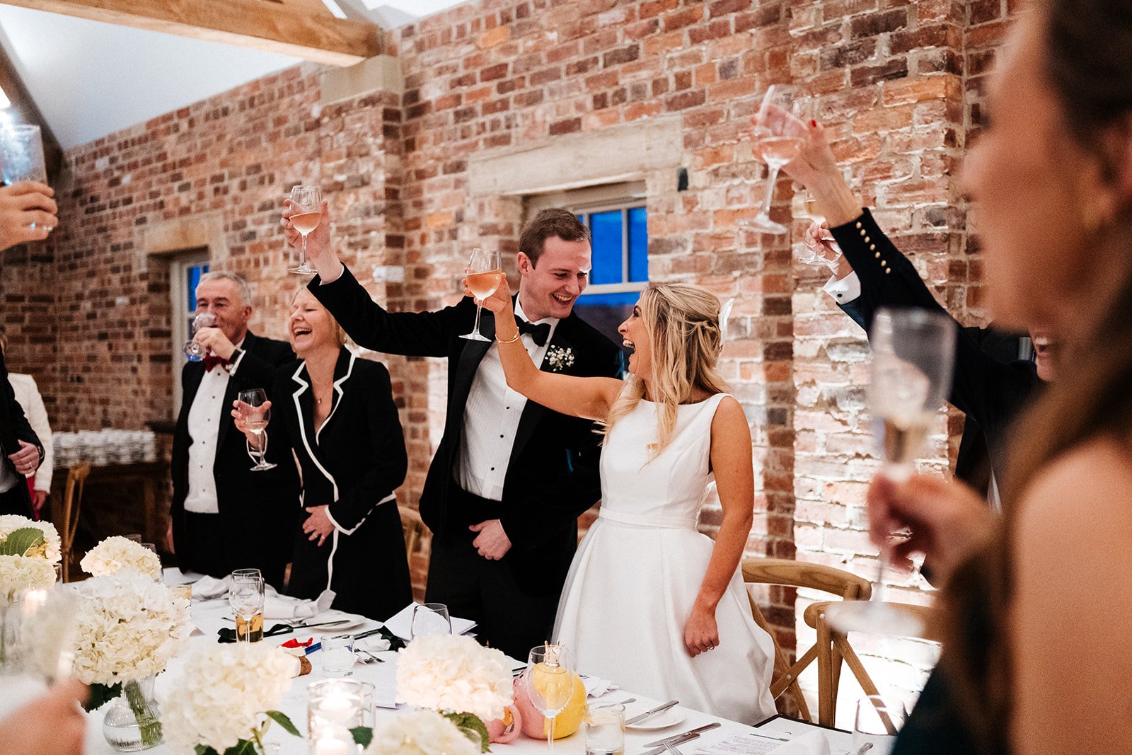 The bride and groom hold a drink in an outstretched arm and smiled at each other during the wedding speeches