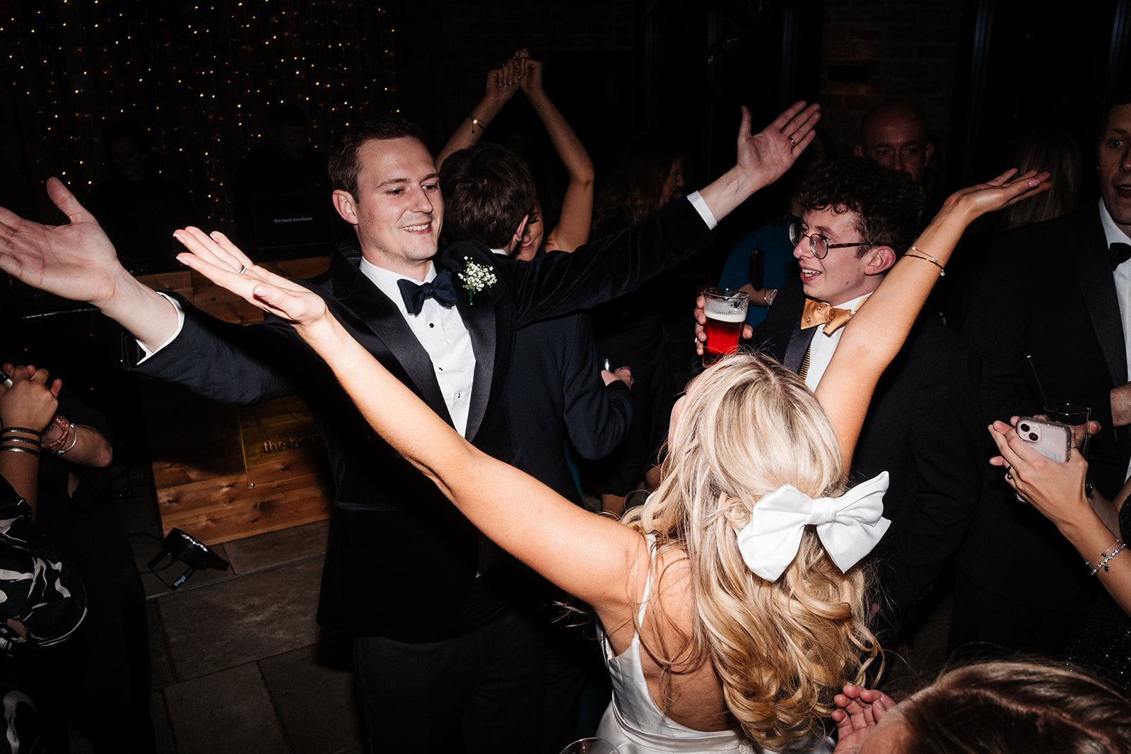 Bride and groom dance together with outstretched arms surrounded by guests