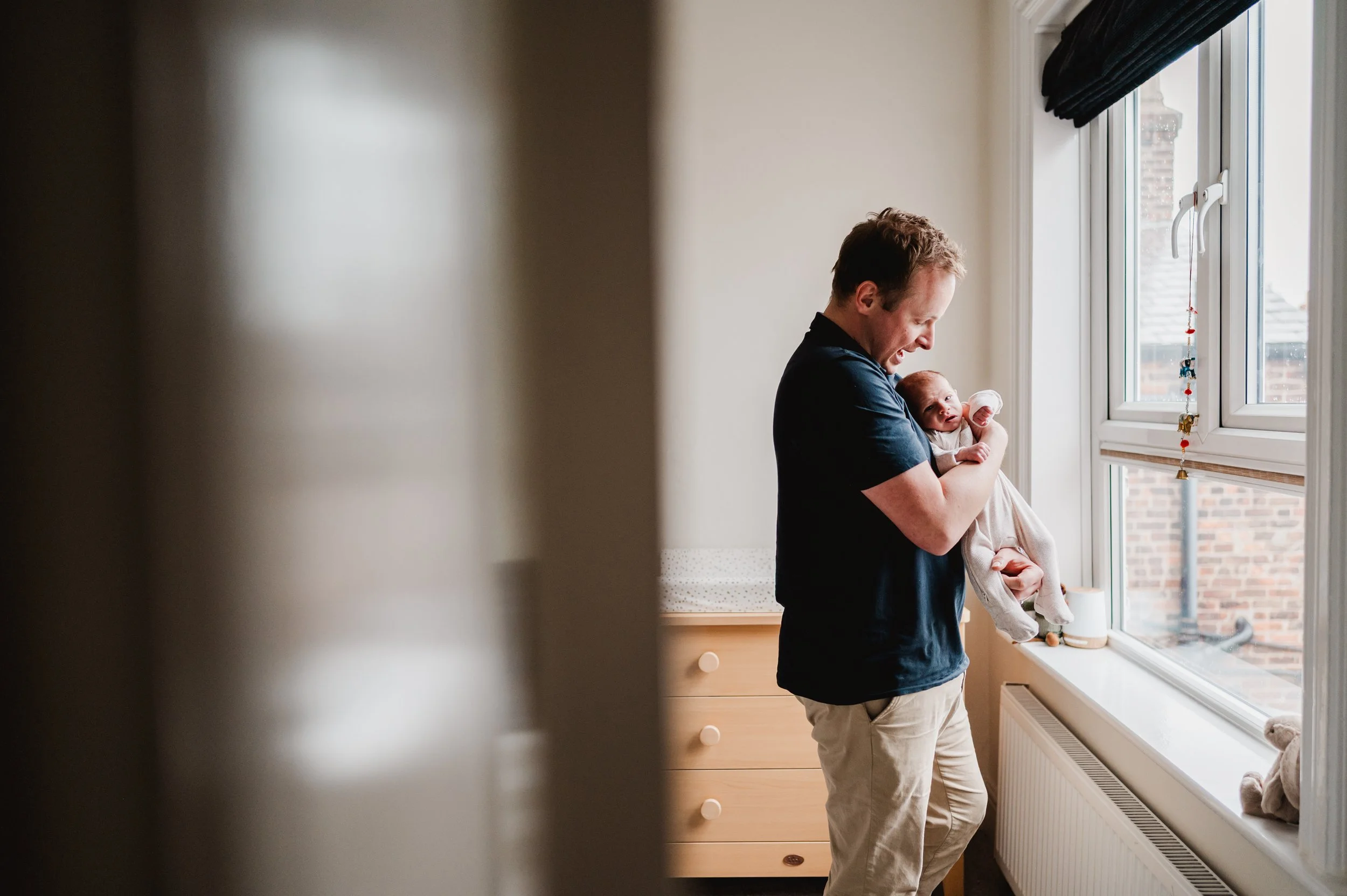 A man holding a baby near a window in a bright room.