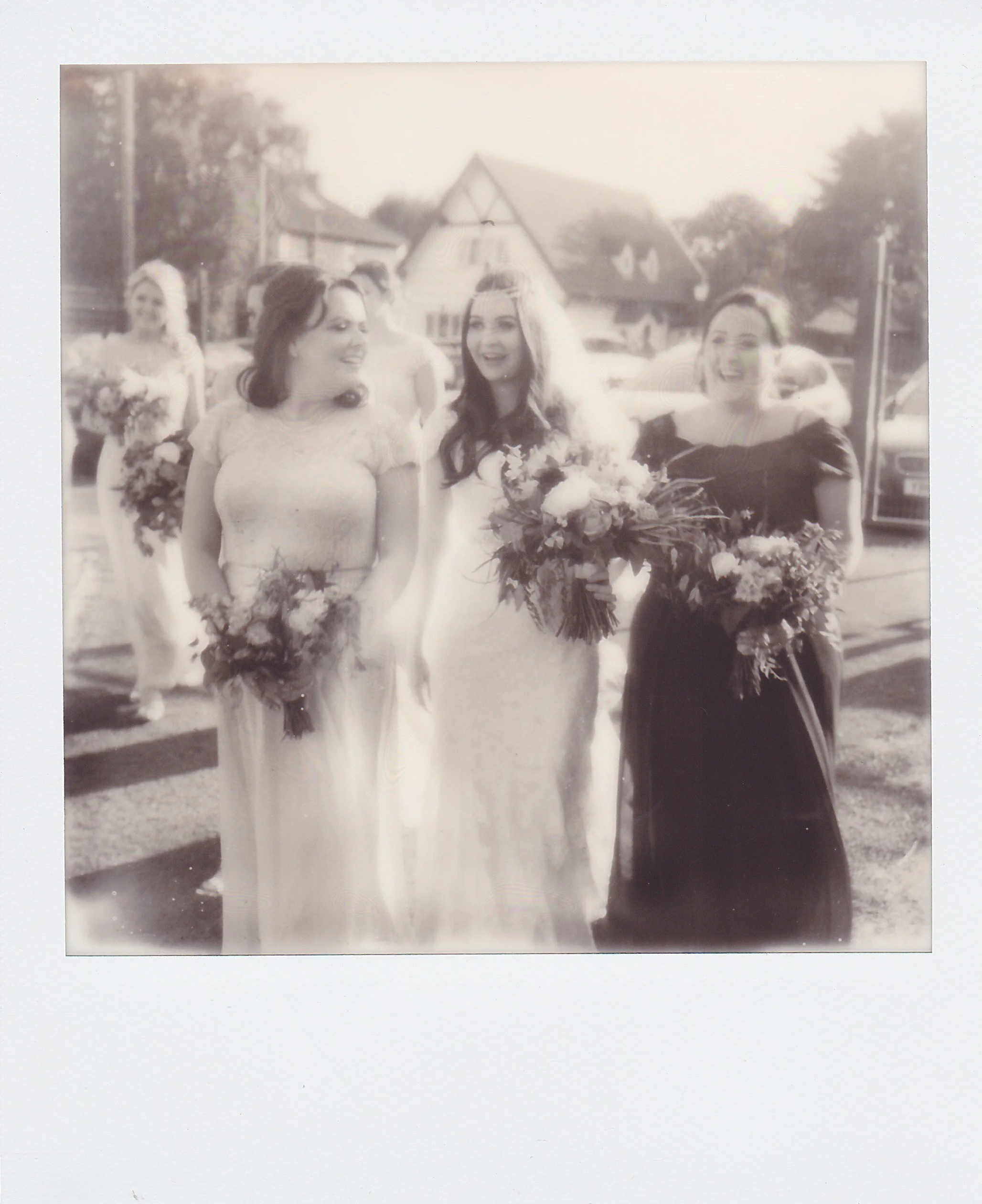 Black and white photograph of a bride with two women, all holding bouquets, standing outside during a wedding celebration.