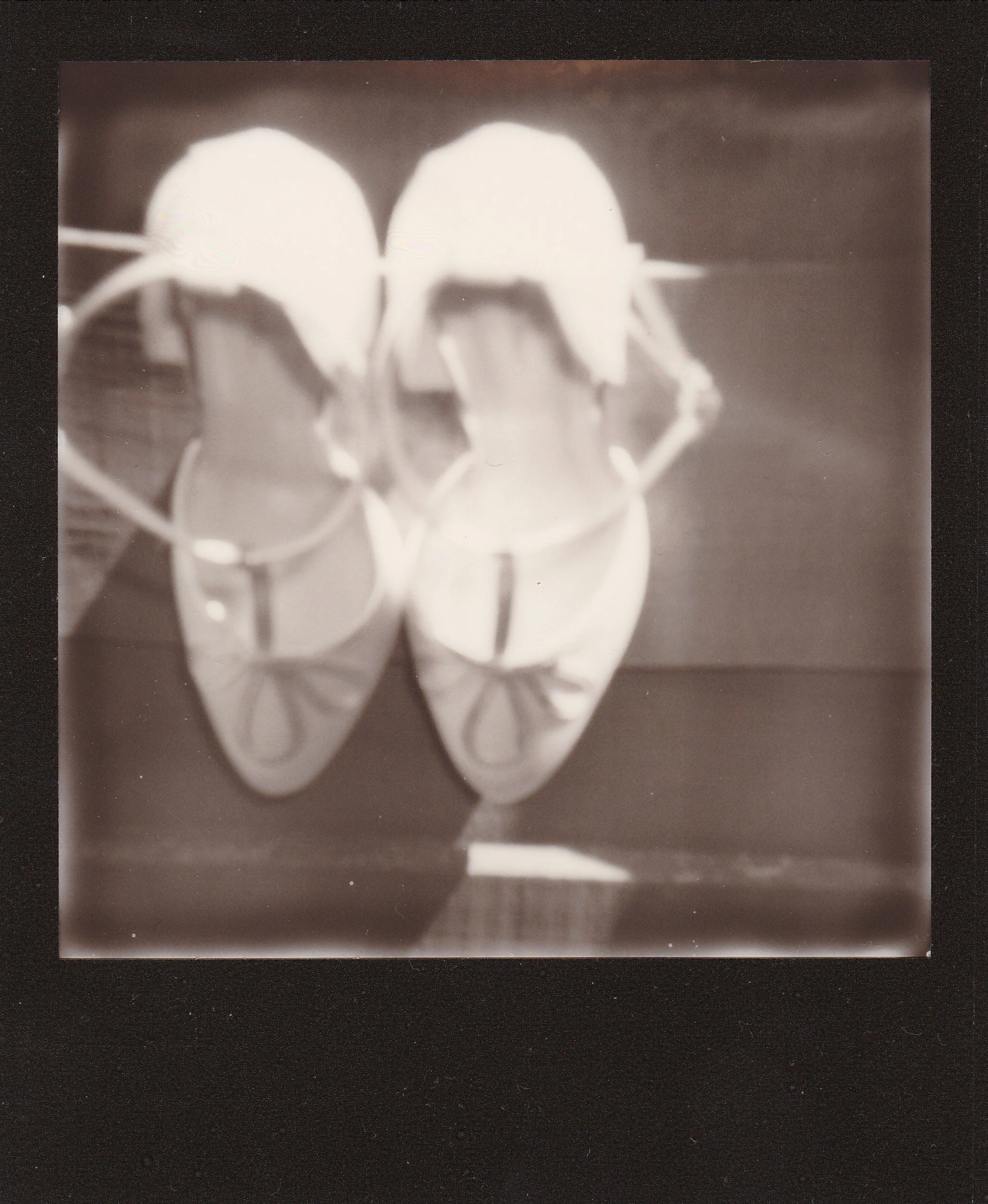 A pair of white ballet slippers on a dark surface, with a reflection visible below.