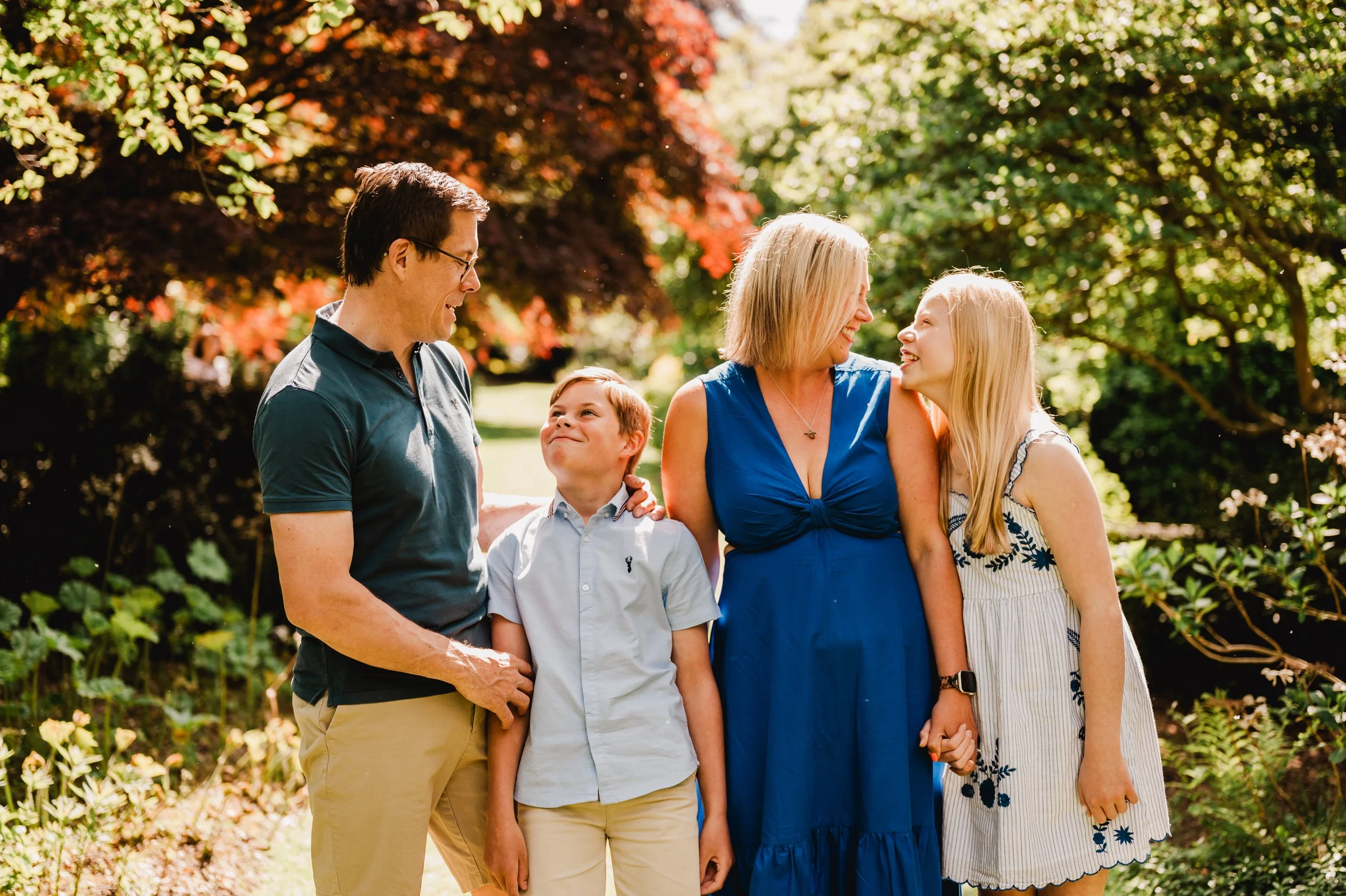 Family of five standing together outdoors in a park with autumn foliage, smiling and holding hands.