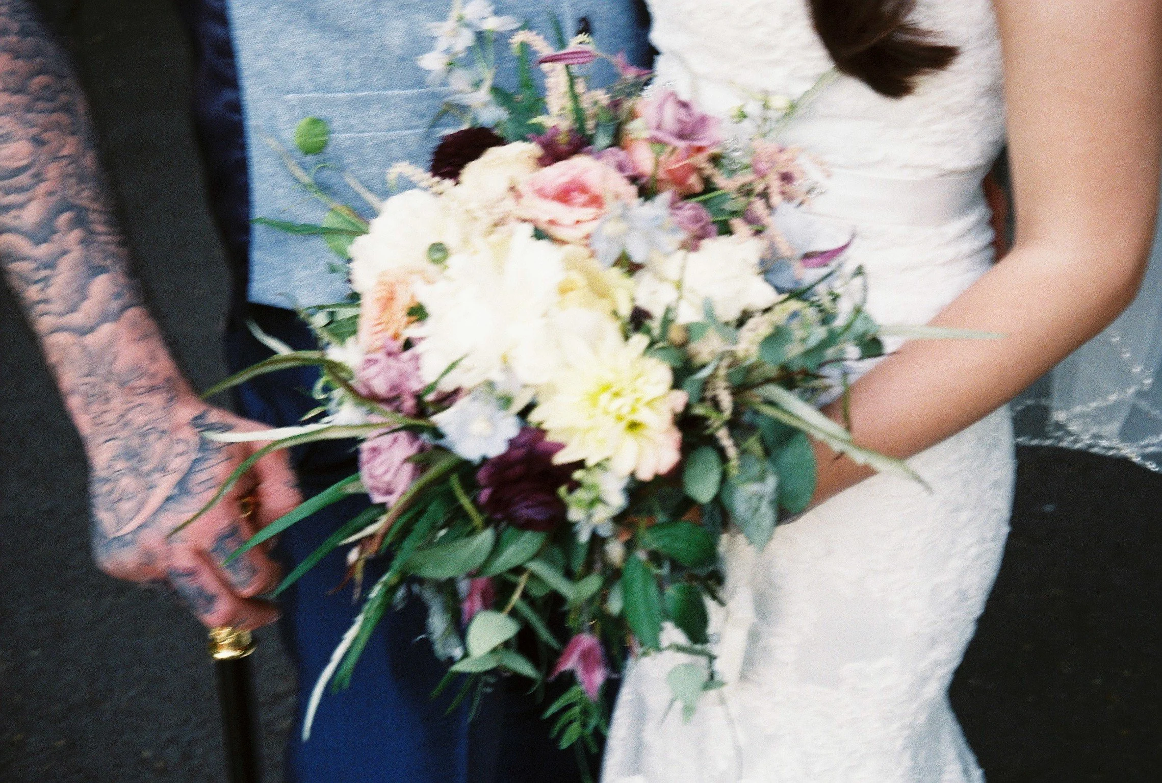 Close-up of a bride holding a floral bouquet with pink, white, purple, and green flowers at a wedding.