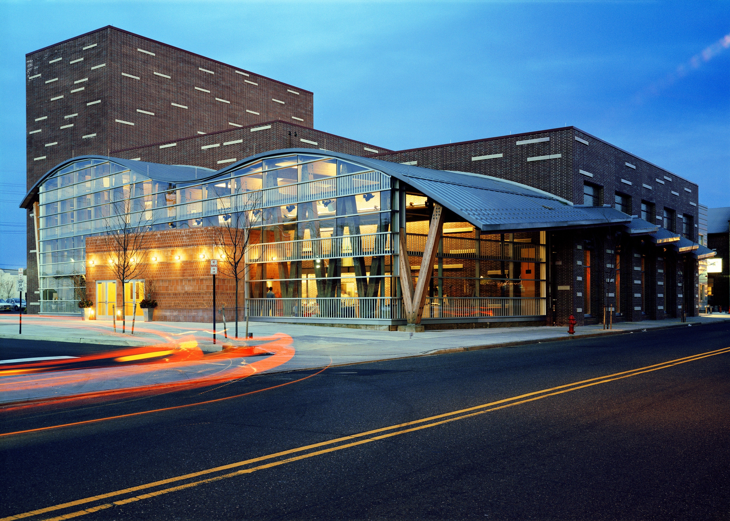 PROJECT: Two River Theater LOCATION: Red Bank, New Jersey CLIENT: Two River Theater Company COMPLETION: 2005 COST: $16.2 Million In 1999, the Two River Theater Company commissioned H3 to design its permanent home. Situated in a former industrial district, the theater’s design responds to its context and is a layering of opposites: raw and finished, transparent and opaque. The theater comprises three forms. The largest is a masonry-clad, 350-seat theater and rehearsal hall. Its patterned, multi-color bricks mimic the surrounding industrial buildings. The second form is a long rectangle, which provides backof-house support and includes dressing rooms, a loading dock, and offices. The third form, the lobby, completes the composition. Sheathed in glass, this two-story volume is accented by wood timbers and, lit at night, acts as a beacon, inviting patrons to enter. On the inside, a curving roof and exposed, diagonal structure, make for a dynamic, playful entry. The theater’s modest thrust stage allows for a range of dramatic productions, and its large proscenium provides a flexible environment for scenic designers. The 2,500-square-foot rehearsal hall doubles as performance space and can also be used for classes and pre- and post performance events.