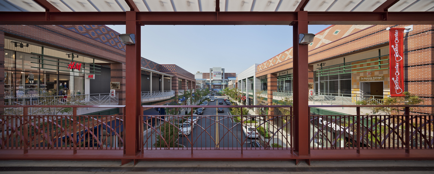 PROJECT: Ridge Hill, Westchester LOCATION: Yonkers, New York CLIENT: Forest City Ratner COMPLETION: 2012 COST: $685 Million Set on a hilltop between the New York State Thruway and Sprain Parkway, Ridge Hill is a new 80-acre, mixed-use town center containing 1.2 million square feet of retail, restaurant, and commercial space, anchored by a twelve-screen cinema complex, department stores, and a 160,000-square-foot office building. In addition to two completed apartment buildings, over a thousand new apartments will be added in future phases. In contrast to the blandness of a typical large-scale outdoor mall, Ridge Hill juxtaposes simplified forms, a variety of materials, and boldly patterned surfaces. This layering of elements is linked by sidewalks and streets to produce the intimate charm of a village without resorting to sentimentality. The development is oriented along an outdoor Main Street that connects several sections of the center. Twenty-one different patterns of colored brick, zinc metal cladding, and translucent polycarbonate skylights provide a framework that creates a vibrant, active backdrop while still allowing maximum flexibility for retailers and restaurants to exhibit their own unique brands. The result is a changing visual tableau that will evolve as time passes. Buildings are varied in scale and fenestration, providing bridges, overlooks, second-floor promenades, and articulated facades to create an arresting series of pedestrian experiences. The Village Green sets the stage for evening entertainment, including a successful serious of summer concerts. During the day, a Tom Otterness playground entertains children and passersby. Plentiful outdoor seating, a dramatic fire-and-water fountain, and a seasonal ice rink offer a variety of amenities to engage visitors throughout the year.