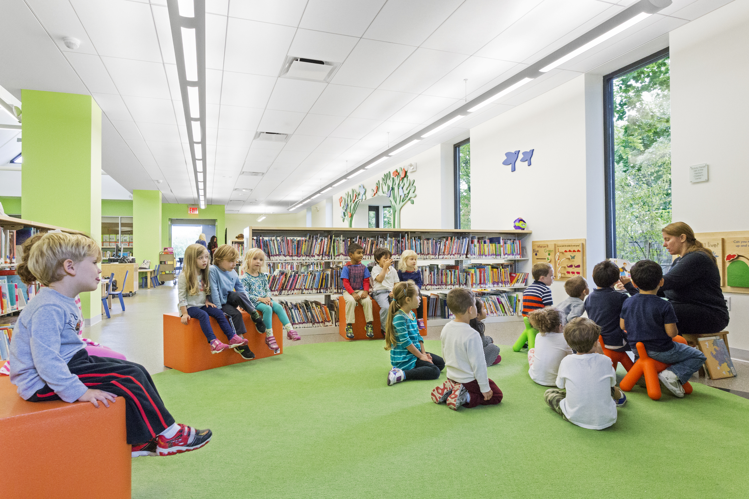 PROJECT: Harrison Public Library LOCATION: Harrison, New York CLIENT: Town Village of Harrison COMPLETION: 2015 SIZE: 15,700 Square Feet COST: $3 Million H3 was hired in 2012 by the Harrison Public Library Trustees to engage in a programming and planning study to determine the need for a library expansion, renovation or both. The Trustees realized that the library’s traditional layout and physical condition was outdated and no longer supported the activities and programming goals. Having recently hired a new Director with roots in the NYPL system, the Trustees were eager to design an active community center appropriate for a contemporary library. Located within the town’s park, the location of the library was ideal, but the existing entrance lacked the presence of a major civic institution. Through analysis and surveys, H3 determined that a re-invigorated Harrison Public Library could best be achieved through minor exterior additions, including a new monumental entry, and major interior re-structuring that would incorporate new programs that had long been desired. Completed in 2015, the design creates a monumental light filled entry patching together the previous additions into a unified vestibule with donor signage and a waiting area. Once inside patrons are welcomed into the lobby with a centrally located circulation area and information wall. An East-West corridor connects each of the designated programming zones with clearly defined entrances and signage for the Children's and Teen's areas. For children, active learning environments include both analog and digital technology to encourage play with an expanded puppet theater and gathering area for group activities. The Children area theme "Garden in the Park" is further emphasized with branch like light fixtures in the clerestory with birds and tree decor on the surrounding walls. The teen area includes both a study area and lounge with bleacher seating with integrated technology for films and gaming. The Adult area occupies the light filled South and East portions of the building that was previously used as offices with new seating areas located at the exterior windows. Community spaces include a community room equipped with new technology for lectures, films, performances and broadcasting, a new learning center and flexible group study spaces. Staff is primarily roaming, with ergonomic seating strategically located in each of the zones to create accessible reference stations.