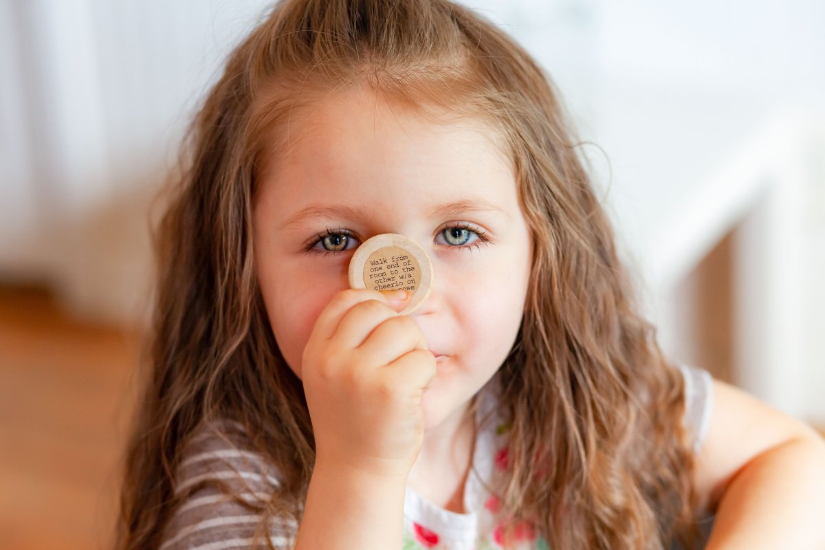 Little Girl Holding a Wooden Coin from an Idea Box Kids Against Her Nose.jpg
