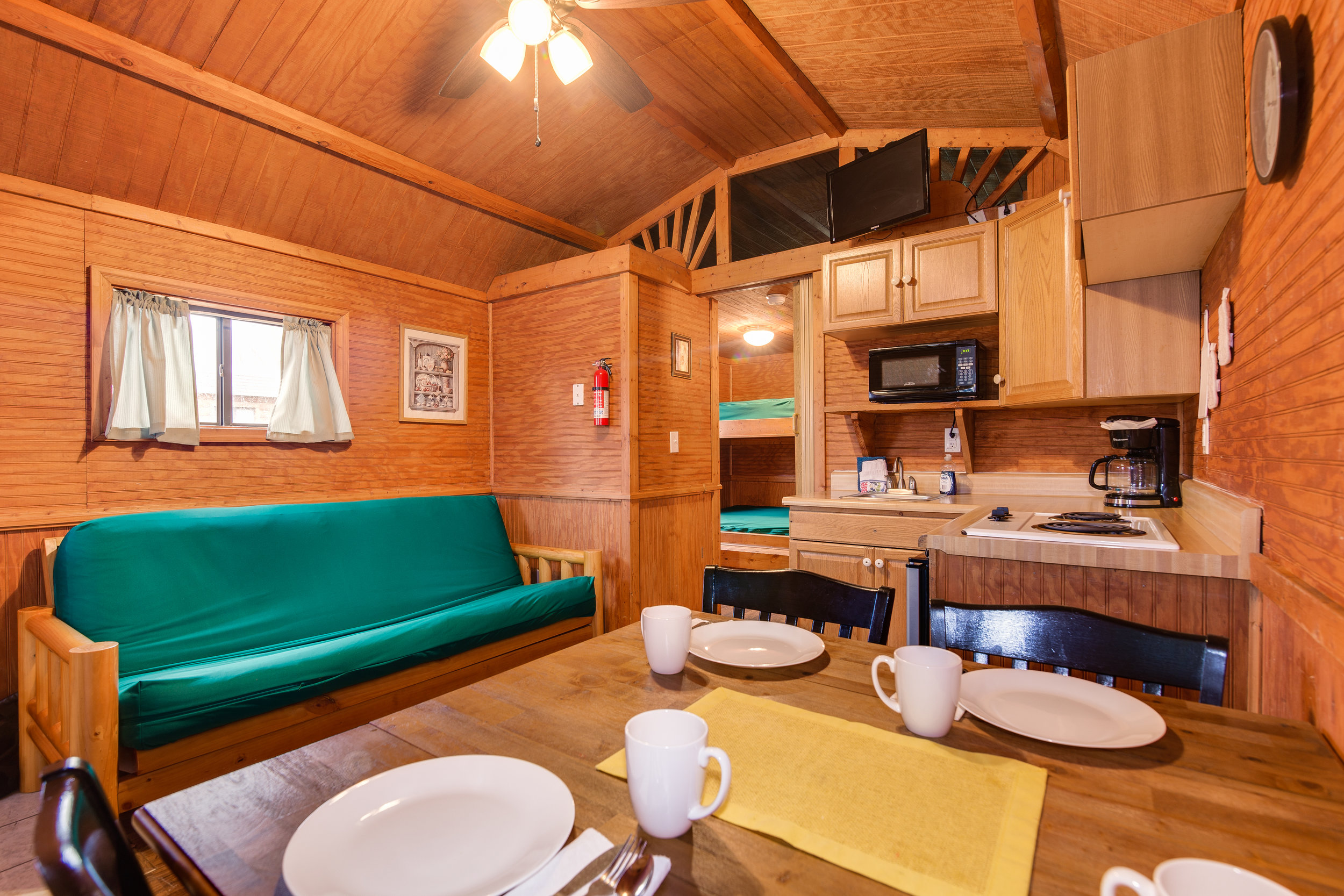  The deluxe cabins feature a futon in the living space, a table and chairs that seat four, and a partial kitchen (pictured). Kitchen linens, pots and pans, glasses, silverware, and dishes are included. There is also a television with campground cable