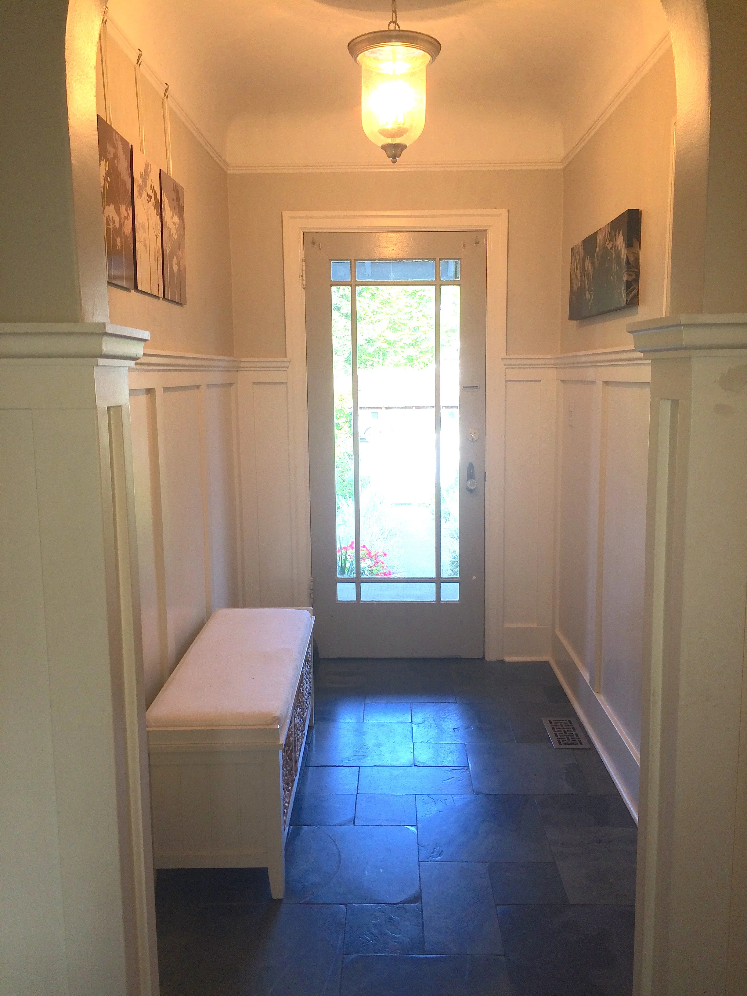 White wainscotting and a vintage style pendant light brighten this formerly dark entrance , while a heated floor of polished slate tile adds comfort & style. 