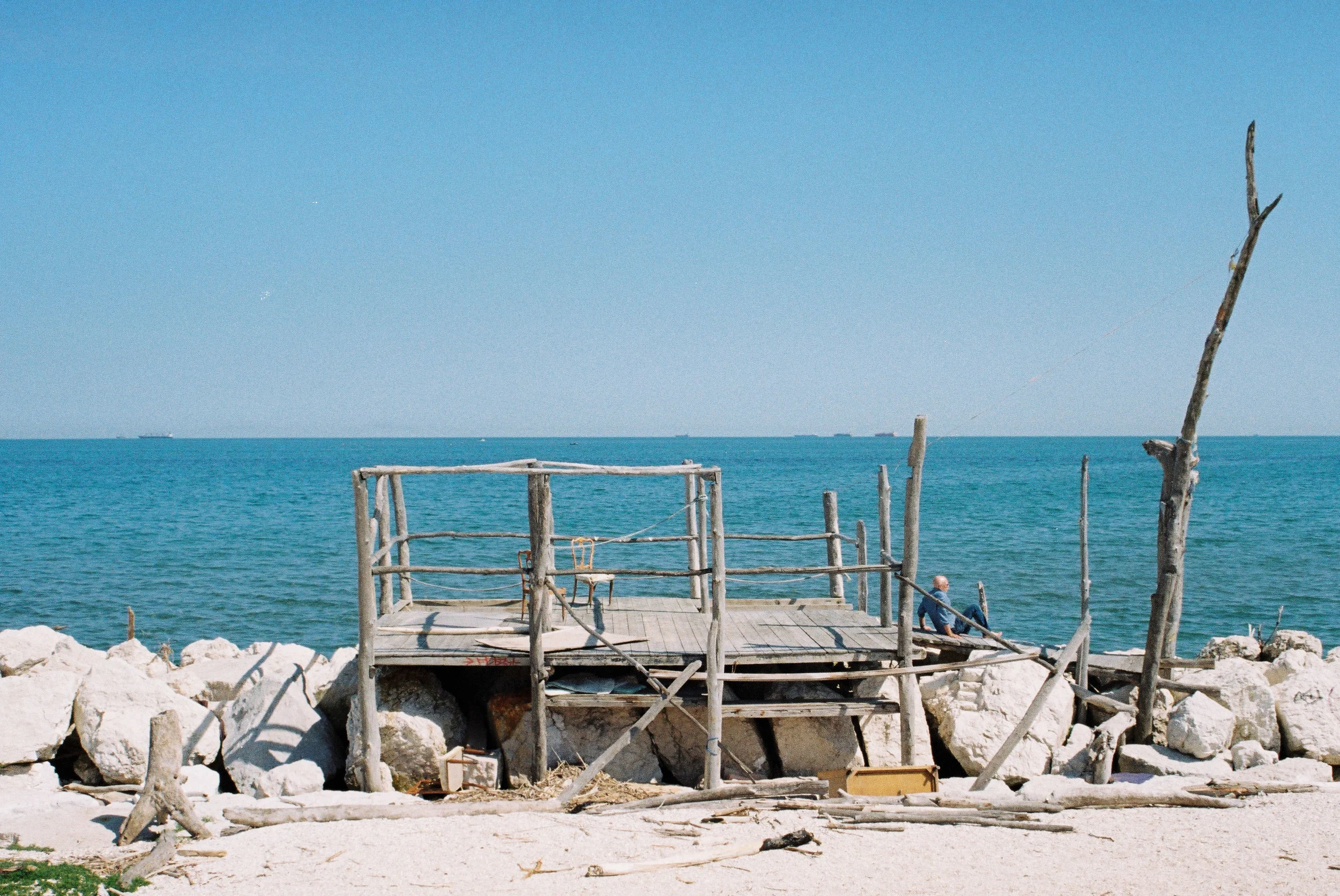  ↑ TEJ BY THE SEA  Location: Venice Lido Medium: Photography  Walking along the Venice Lido coast, away from the tourist beach, stone groynes project out into the Adriatic Sea. Over the years locals have contributed their own additions to this landsc