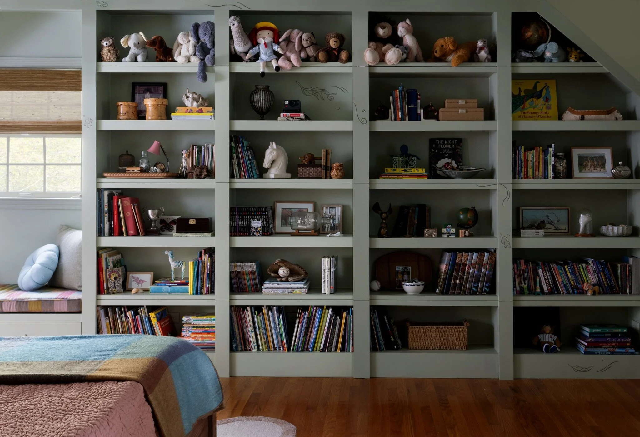 I designed this custom bookshelf wall in the Fantasy Twins Suite to work hard&mdash;hold a lot of twin-sized stuff, offer cord cut-outs for electronics, make space for a cozy window seat (obviously) and hardest of all: hide a secret door to their pla