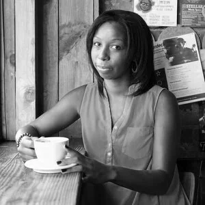 Woman sitting at a wooden table in a cafe, holding a cup.