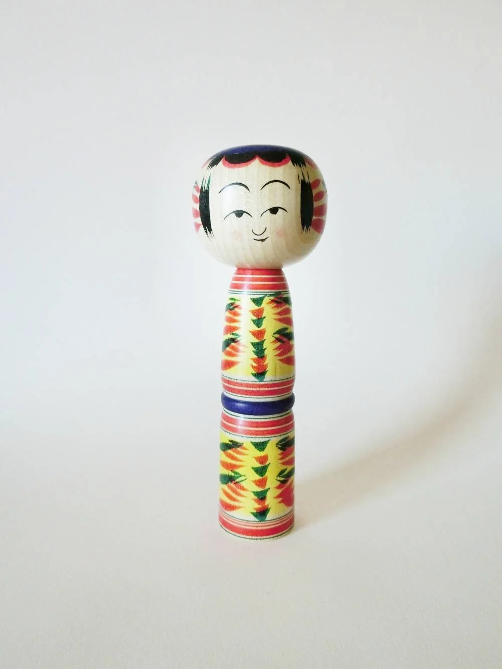 Yajiro kokeshi doll with yellow background, by Kamata Takashi