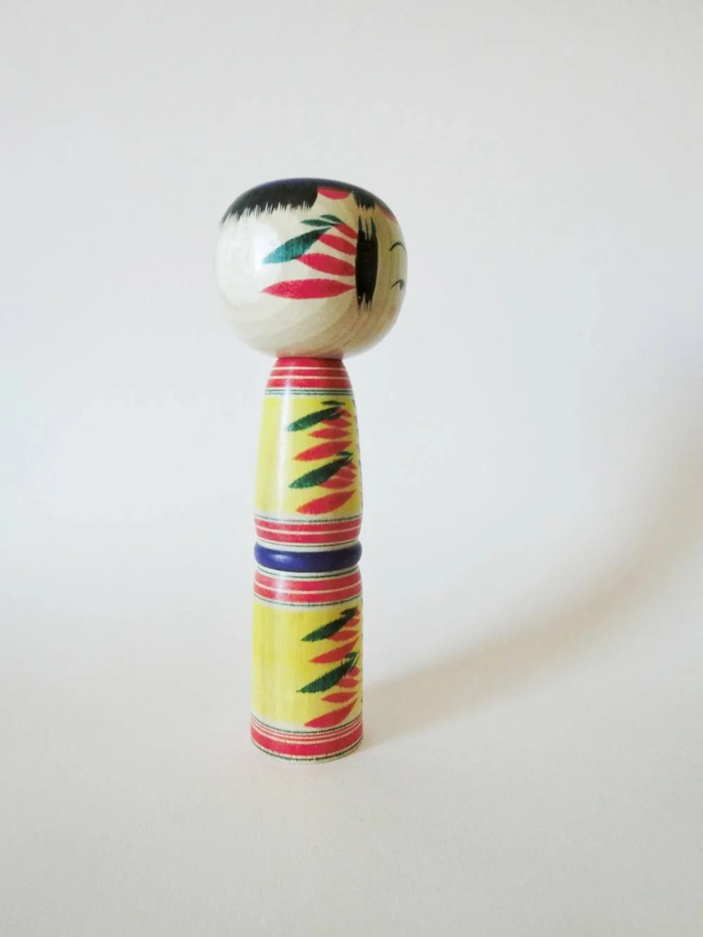 Yajiro kokeshi doll with yellow background, by Kamata Takashi