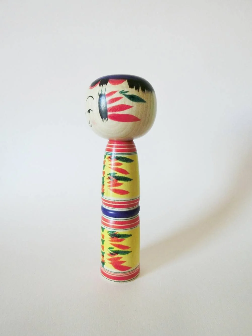Yajiro kokeshi doll with yellow background, by Kamata Takashi
