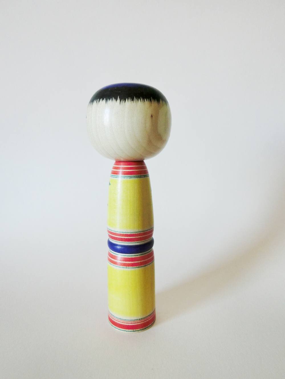 Yajiro kokeshi doll with yellow background, by Kamata Takashi