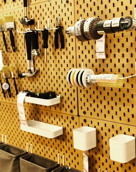 A close up photo of an IKEA display with a variety of workshop tools and hanging containers on a brown peg-board modular wall.