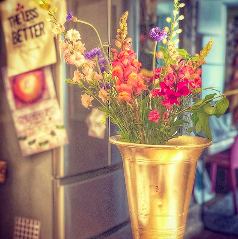 A close up photograph of wildflowers in a gold vase against a kitchen backdrop.