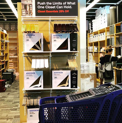 A crisp photograph of the closet section of the Container Store. With a sign that says “push the limits of what one closet can hold.”