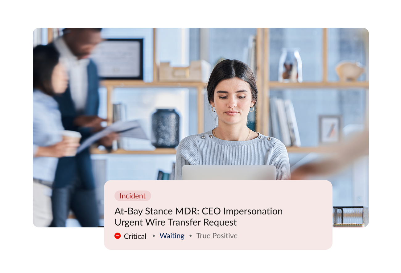 A woman sitting at a desk working on a laptop, with two colleagues standing in the background. A digital alert overlay indicates an incident related to a CEO impersonation phishing attempt, marked as critical, waiting, and true positive.
