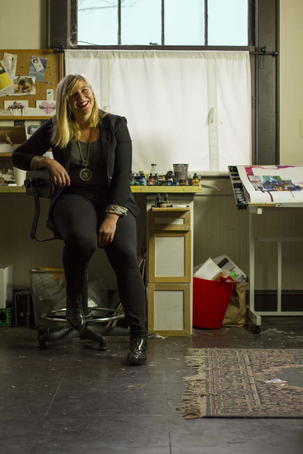 Ursula smiling sitting on a stool in her studio