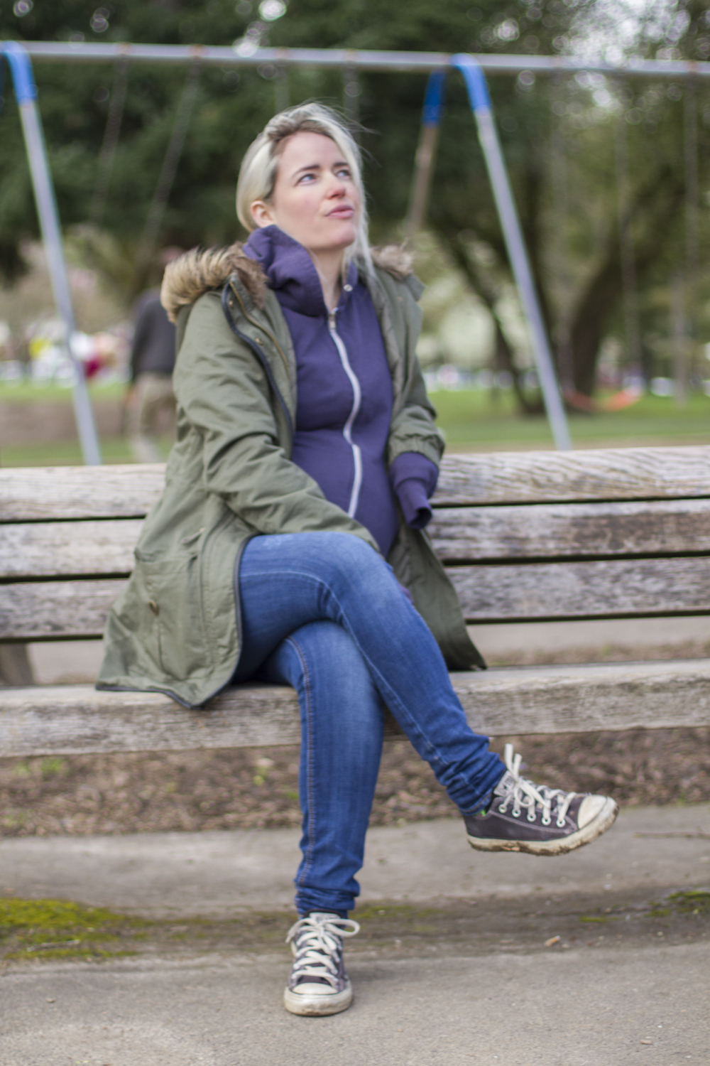 Megan sitting on a park bench looking towards the sky with a pregnant belly