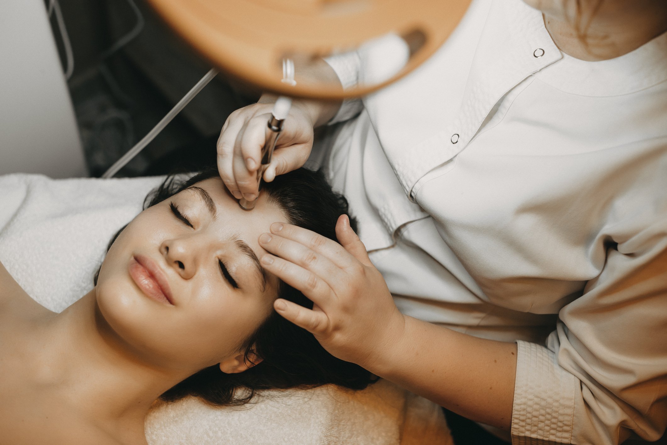 A woman receiving a cosmetic or medical treatment on her forehead from a professional in a clinical setting.