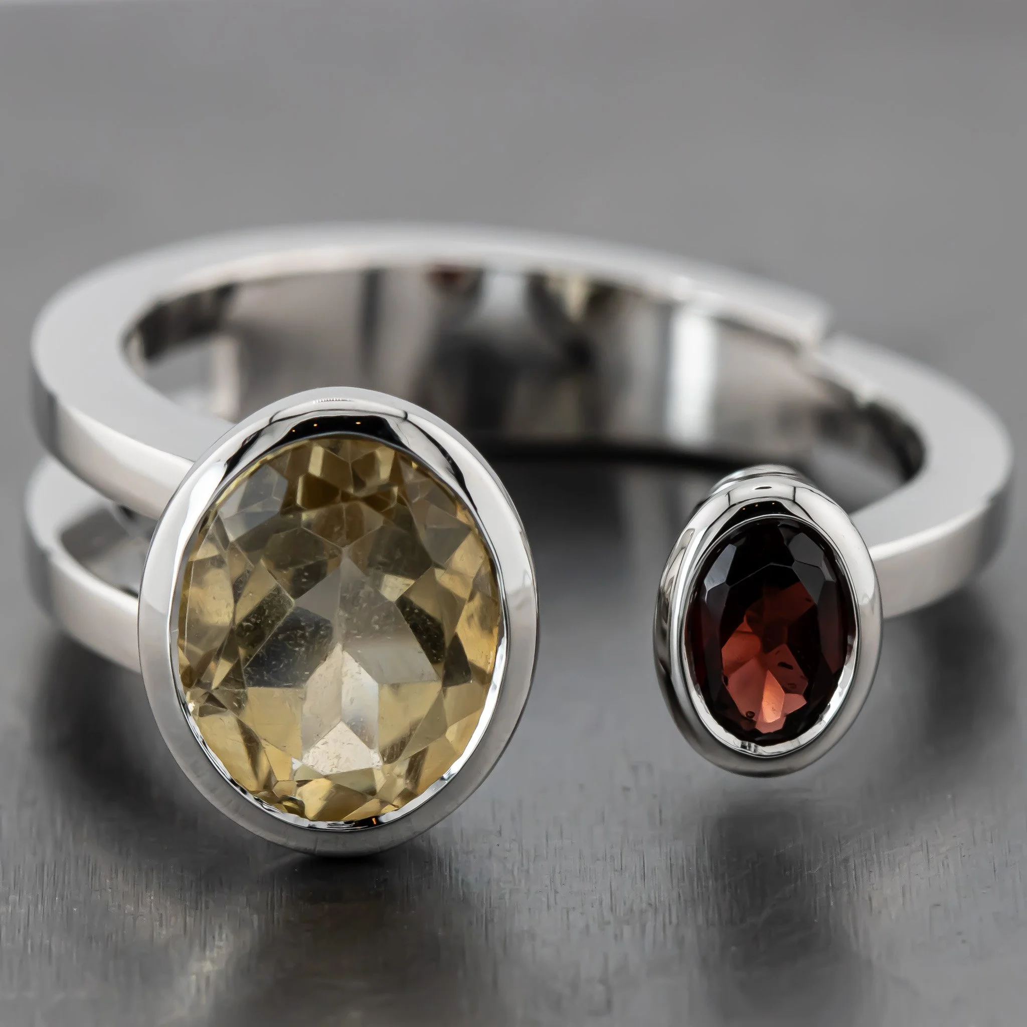 Close-up of a silver ring with a large, faceted, yellow gemstone set in it, placed on a metallic surface.