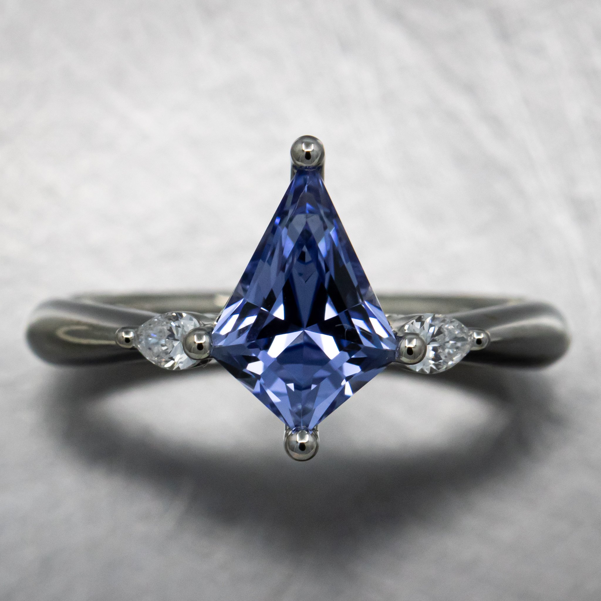 CUSTOM ENGAGEMENT RING : Features a Custom-Shield-Cut Laboratory Grown Cornflower Blue Sapphire in 14k White Gold with a Pear Shape Laboratory Grown Diamond on either side of the Center Stone