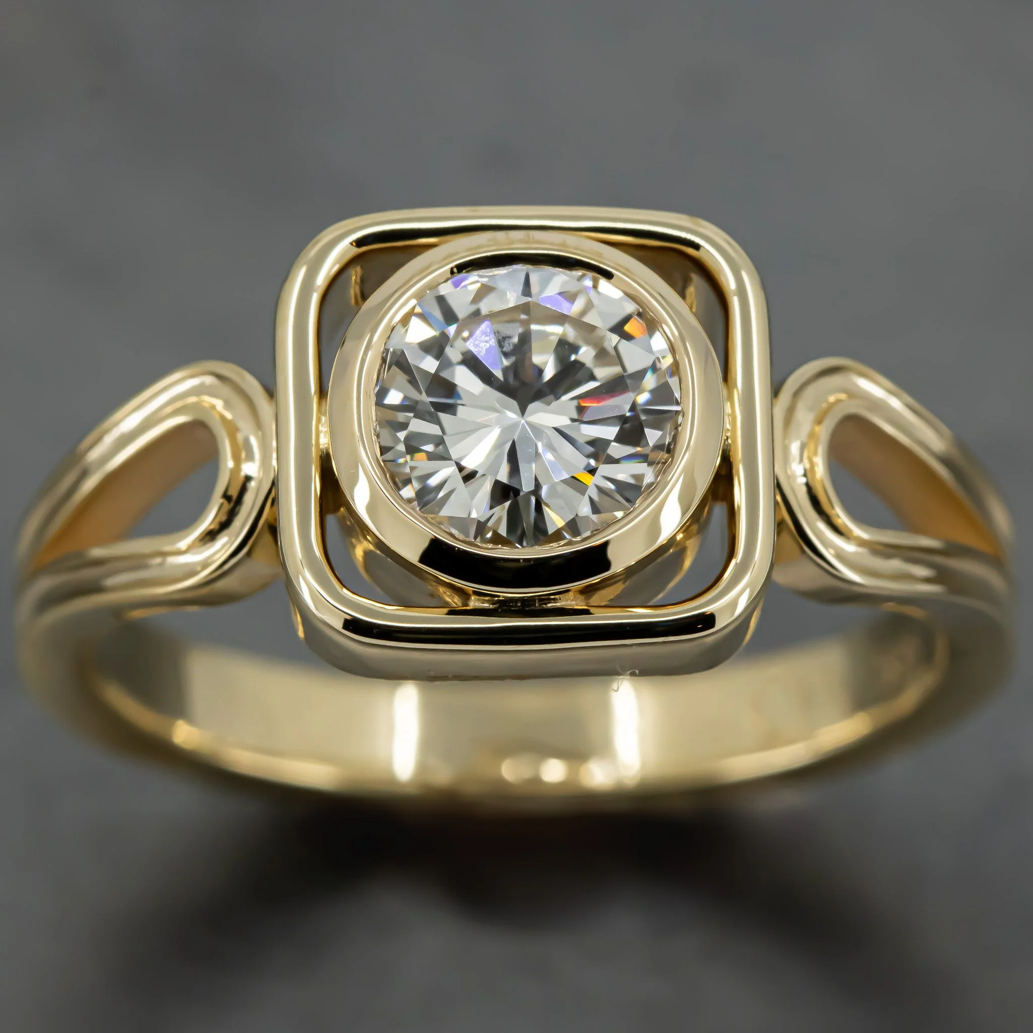 Gold ring with a large round diamond set in a square-shaped gold frame.