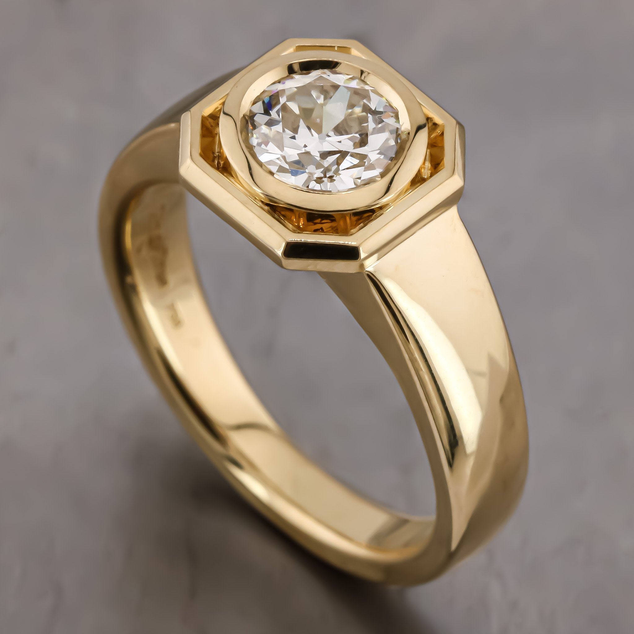 Close-up of a gold ring with a large round diamond in the center, held in a subtle hexagonal setting.