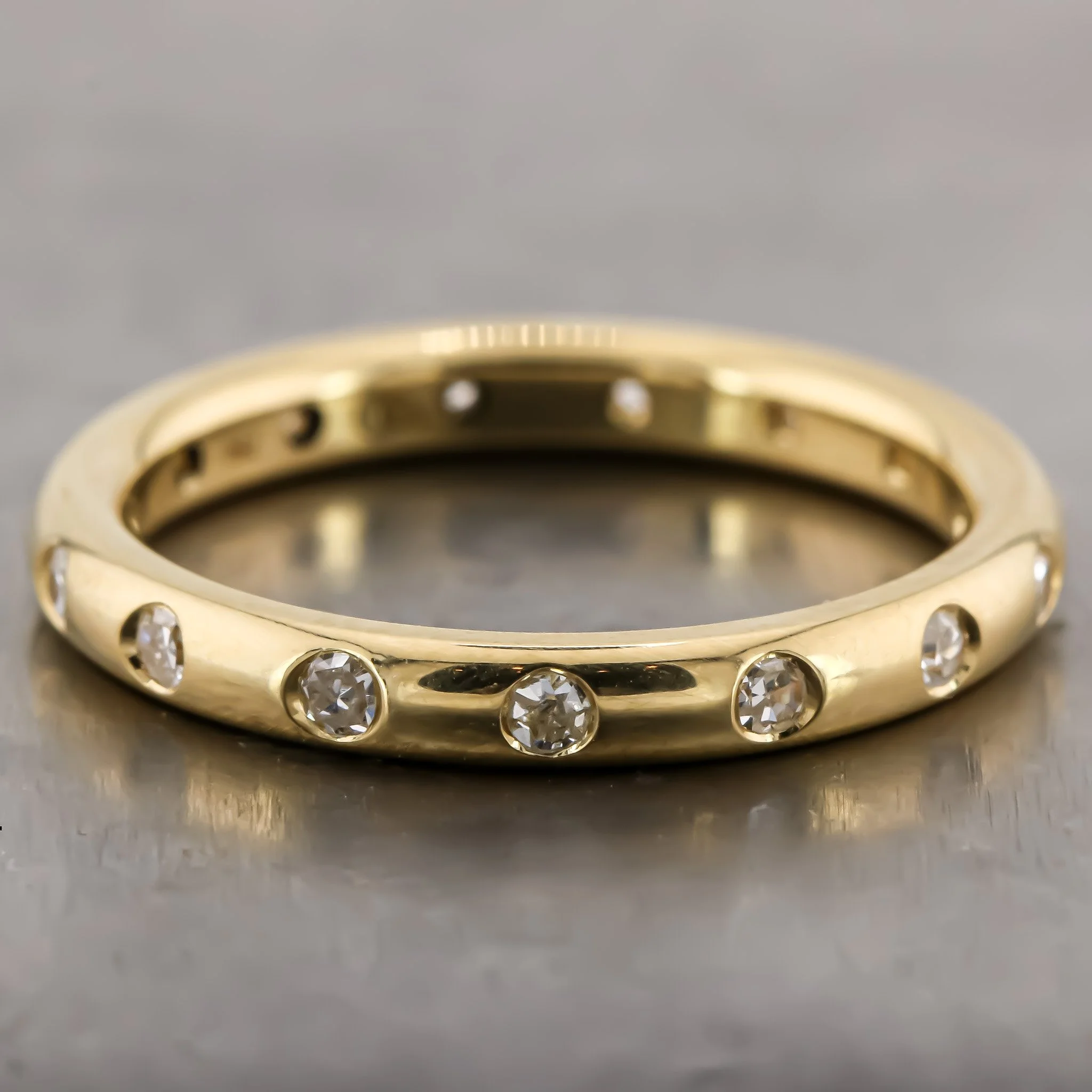 Close-up of a gold ring with embedded diamonds, shown against a gray background.