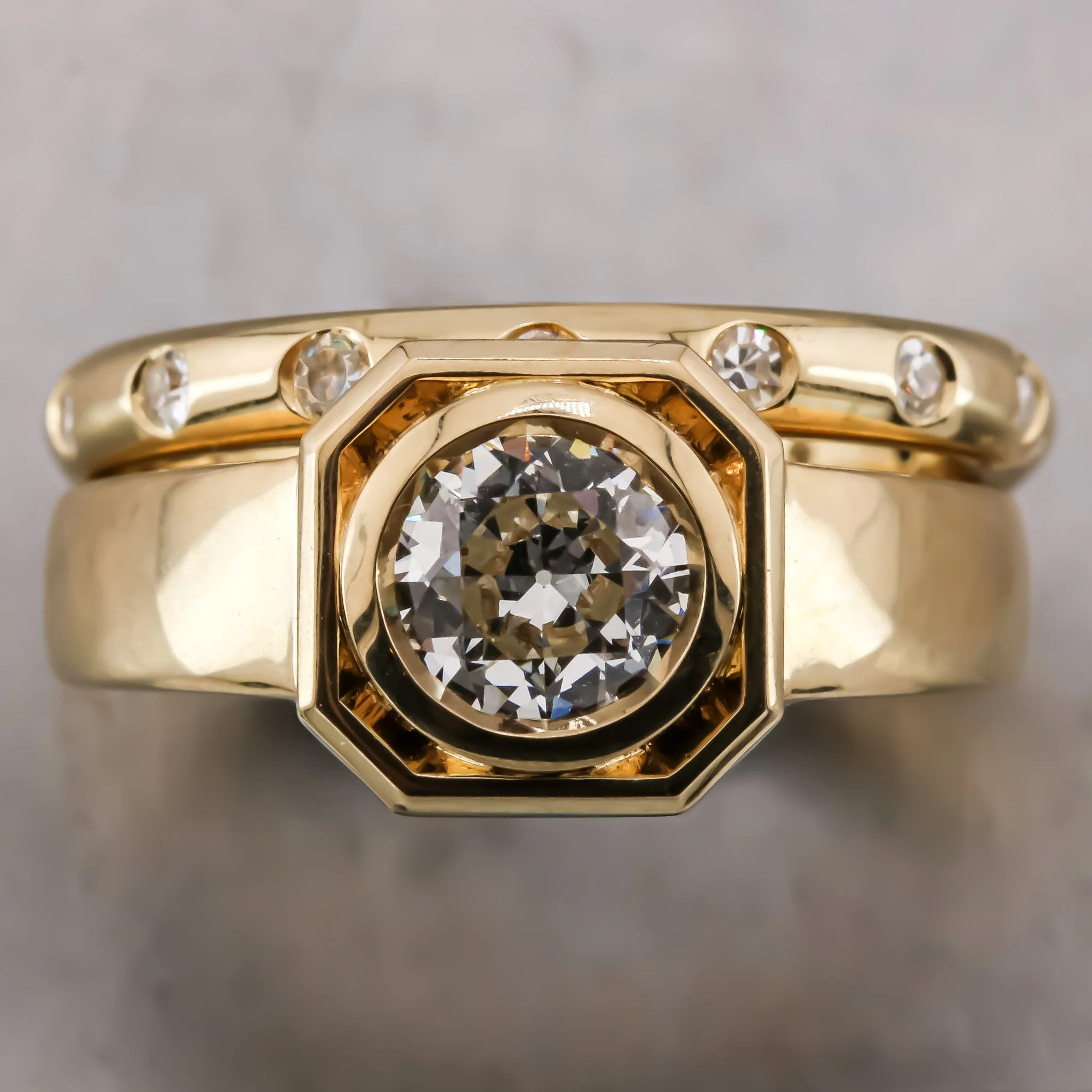 Close-up of a gold ring with a large round diamond and smaller diamonds surrounding it, set against a plain background.