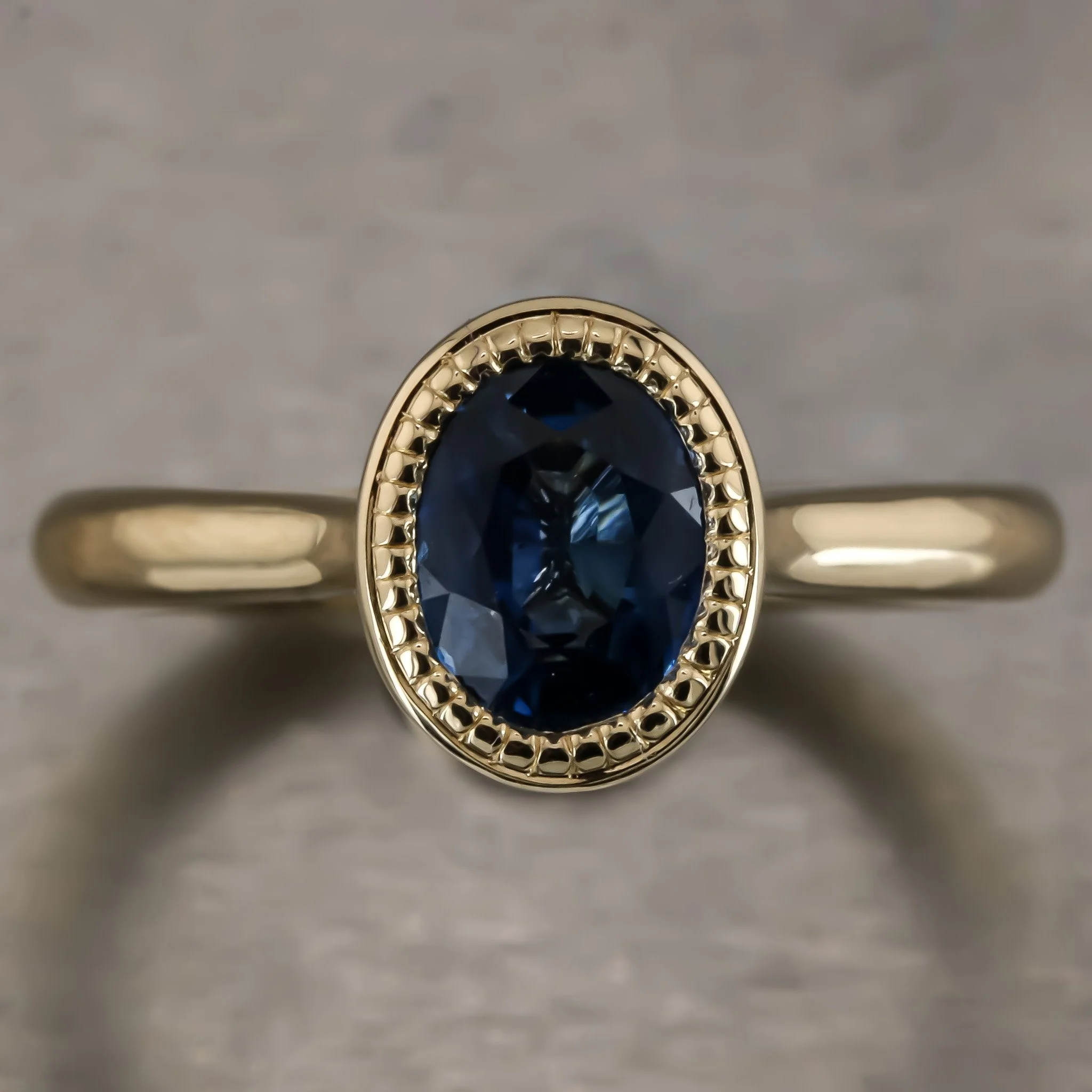 Gold ring with an oval dark blue gemstone surrounded by a decorative gold bezel.