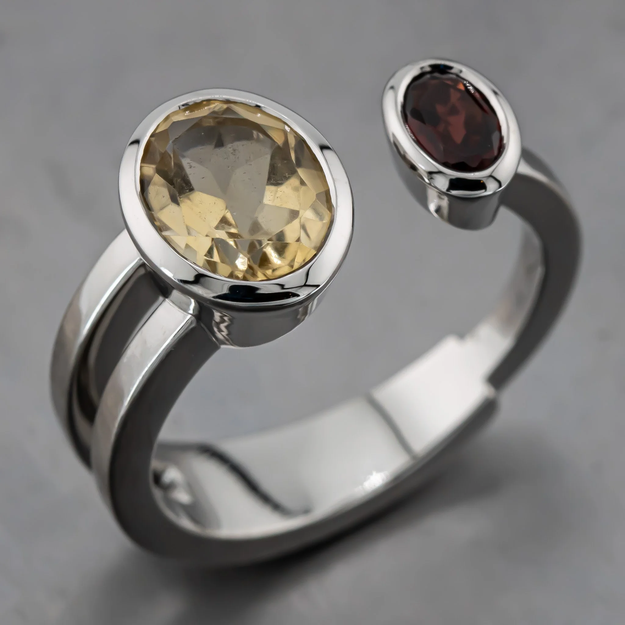 Close-up of two rings with large, oval gemstones, one with a yellow gemstone and the other with a dark red gemstone, set in silver, on a grey surface.