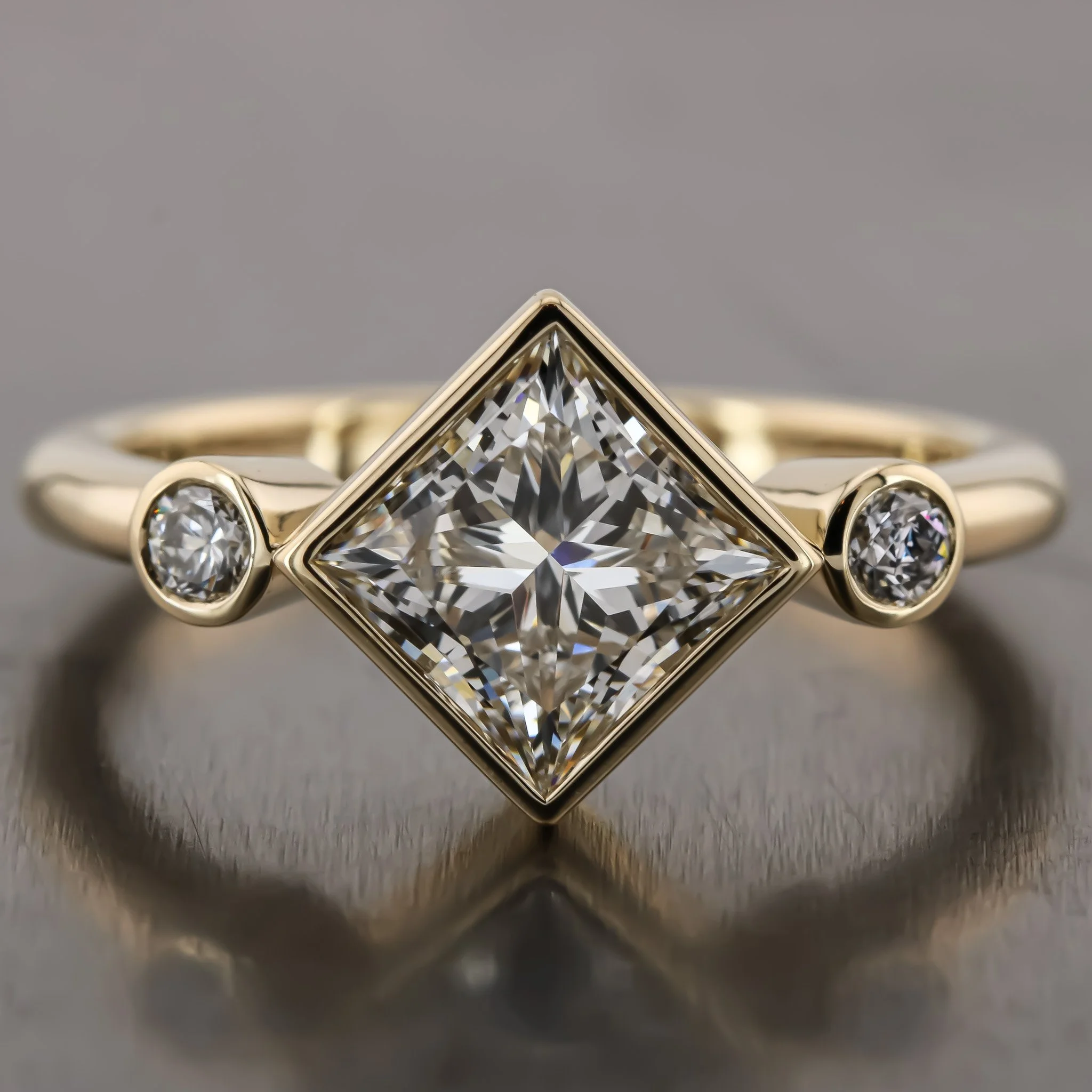 A gold ring with two small round diamonds on either side of a large square-cut diamond.