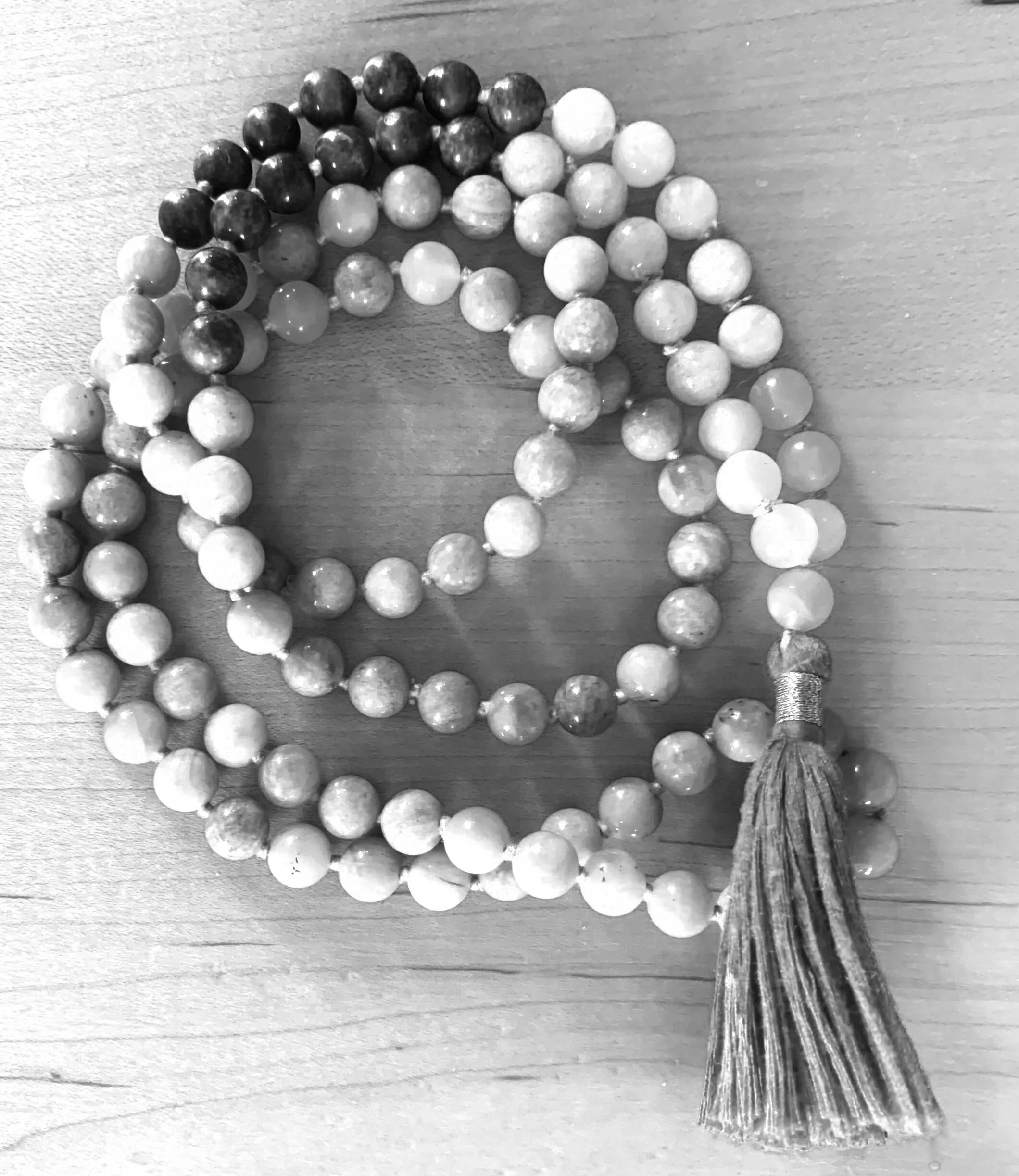 Black and white photo of a beaded necklace with large, round beads and a tassel at the end on a wooden surface.