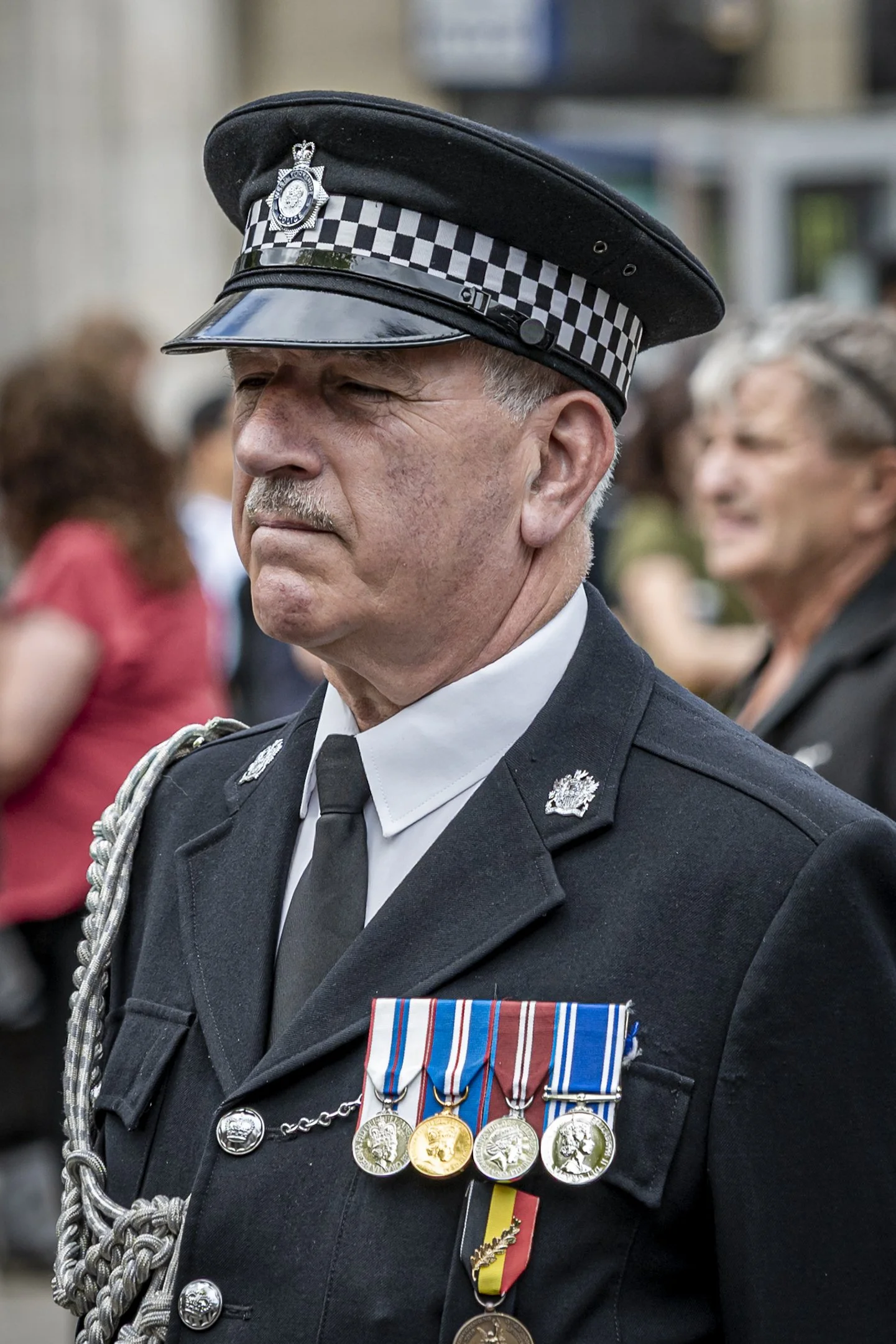 A police officer in uniform with medals and decorations, standing among a crowd of people at a public event.