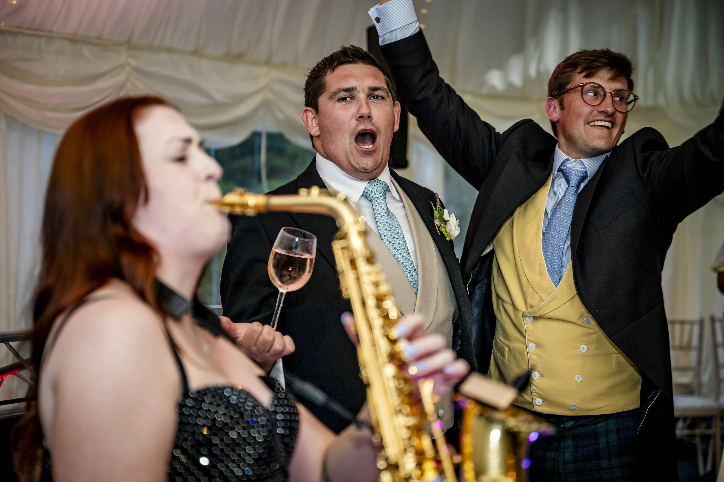 People at a wedding celebration, one playing saxophone, others dancing and enjoying the moment.