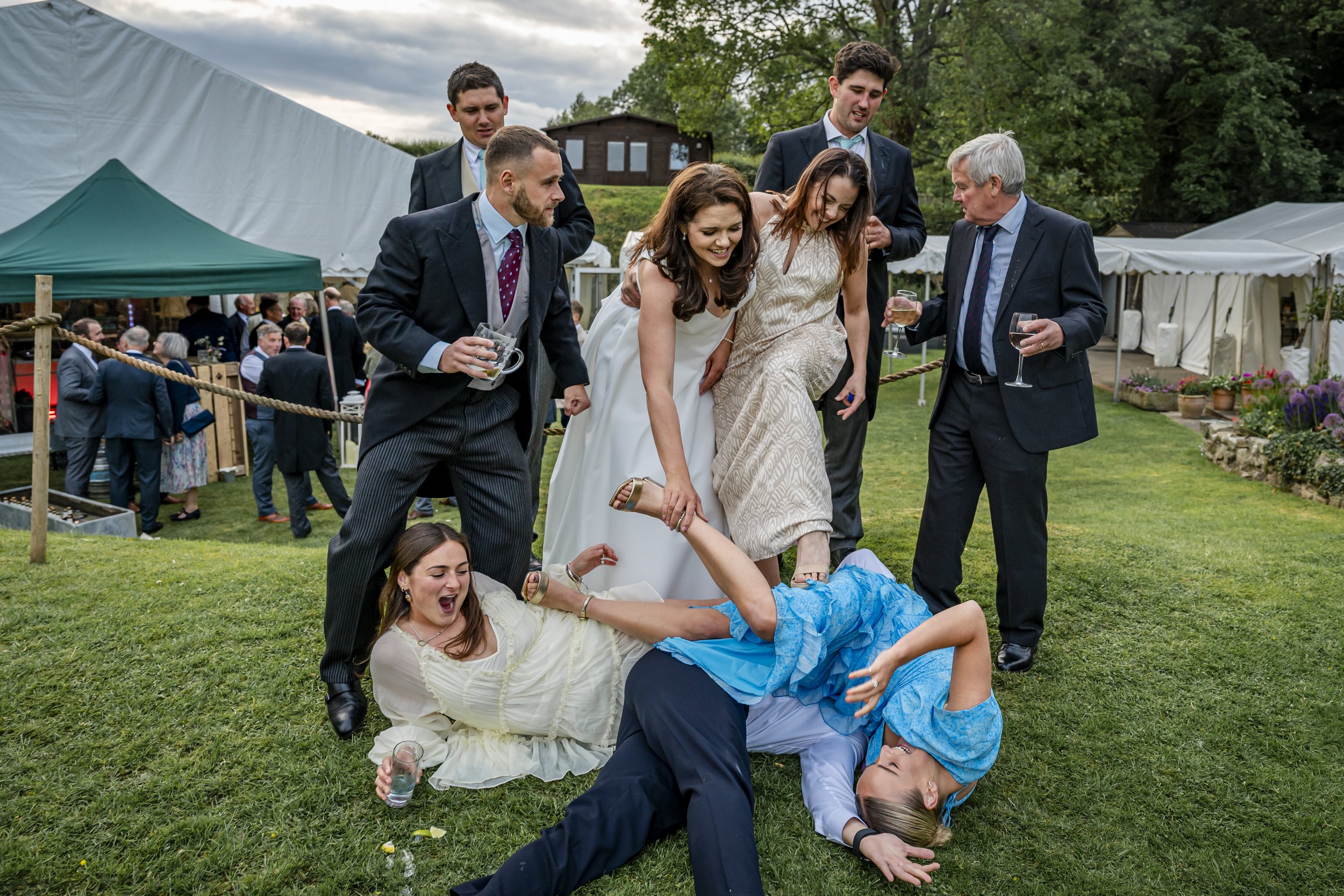 People dancing and celebrating at an outdoor wedding reception, with a tent and garden in the background.