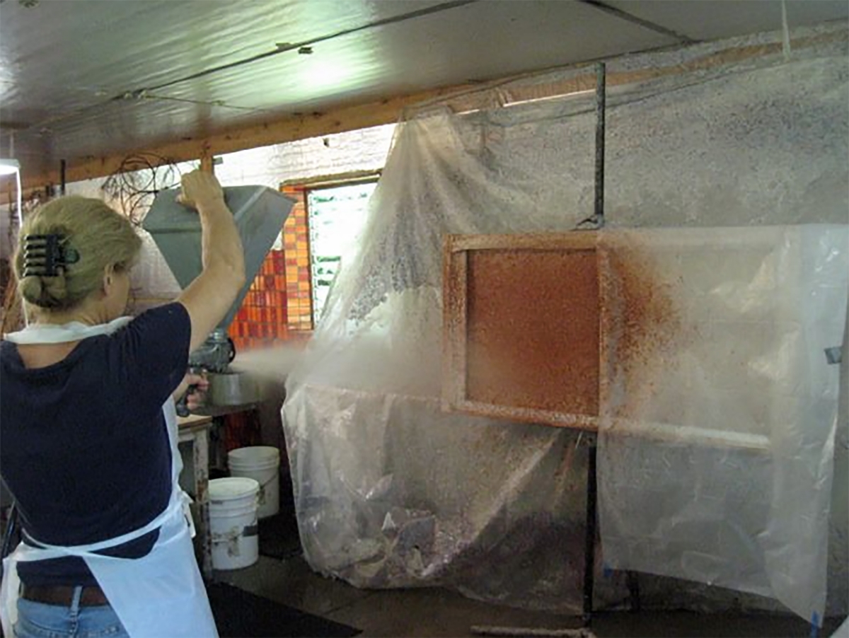 Gigi is spraying colored pulp on half of her paper piece.