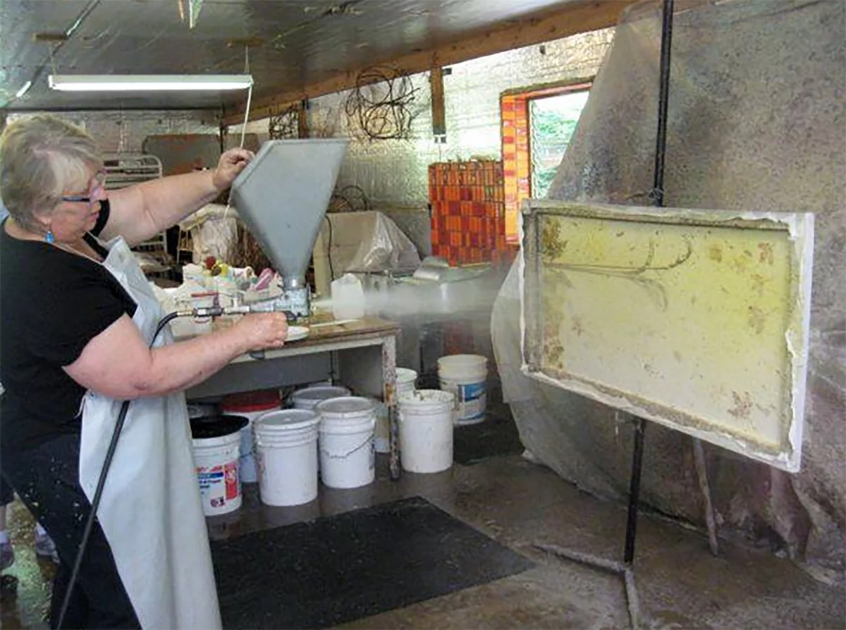 Kay is spraying another layer of pulp on her paper piece with plant inclusions between the layers.