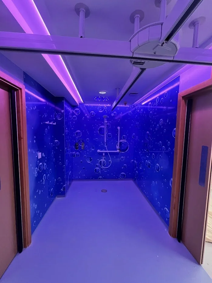 Hospice shower room with blue water bubbles image cladding to walls, and pink feature lighting.