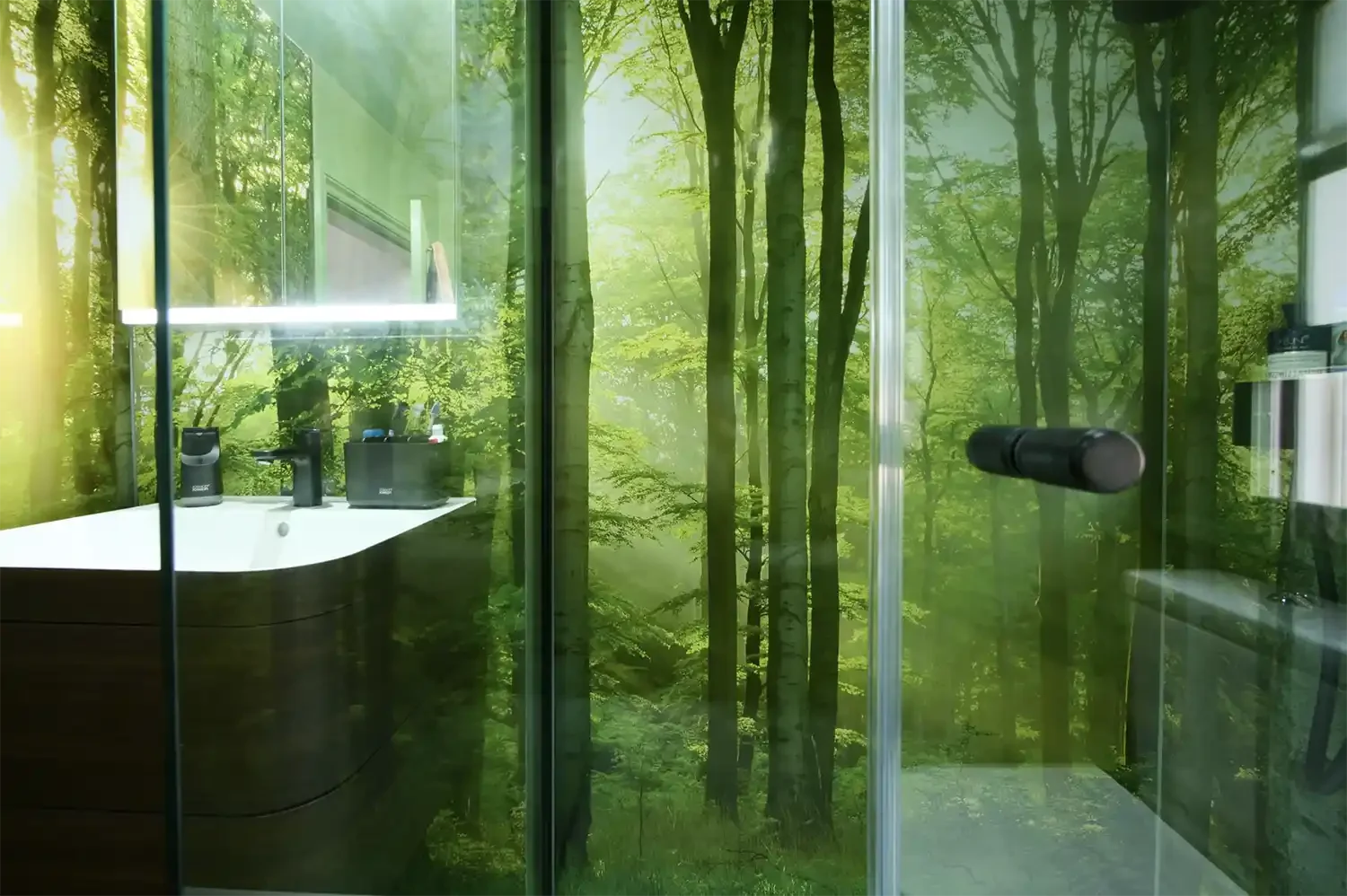 Photo of shower area of a modern bathroom with wrap-around wall panels with lush green forest imagery. sliding glass shower screen in foreground.