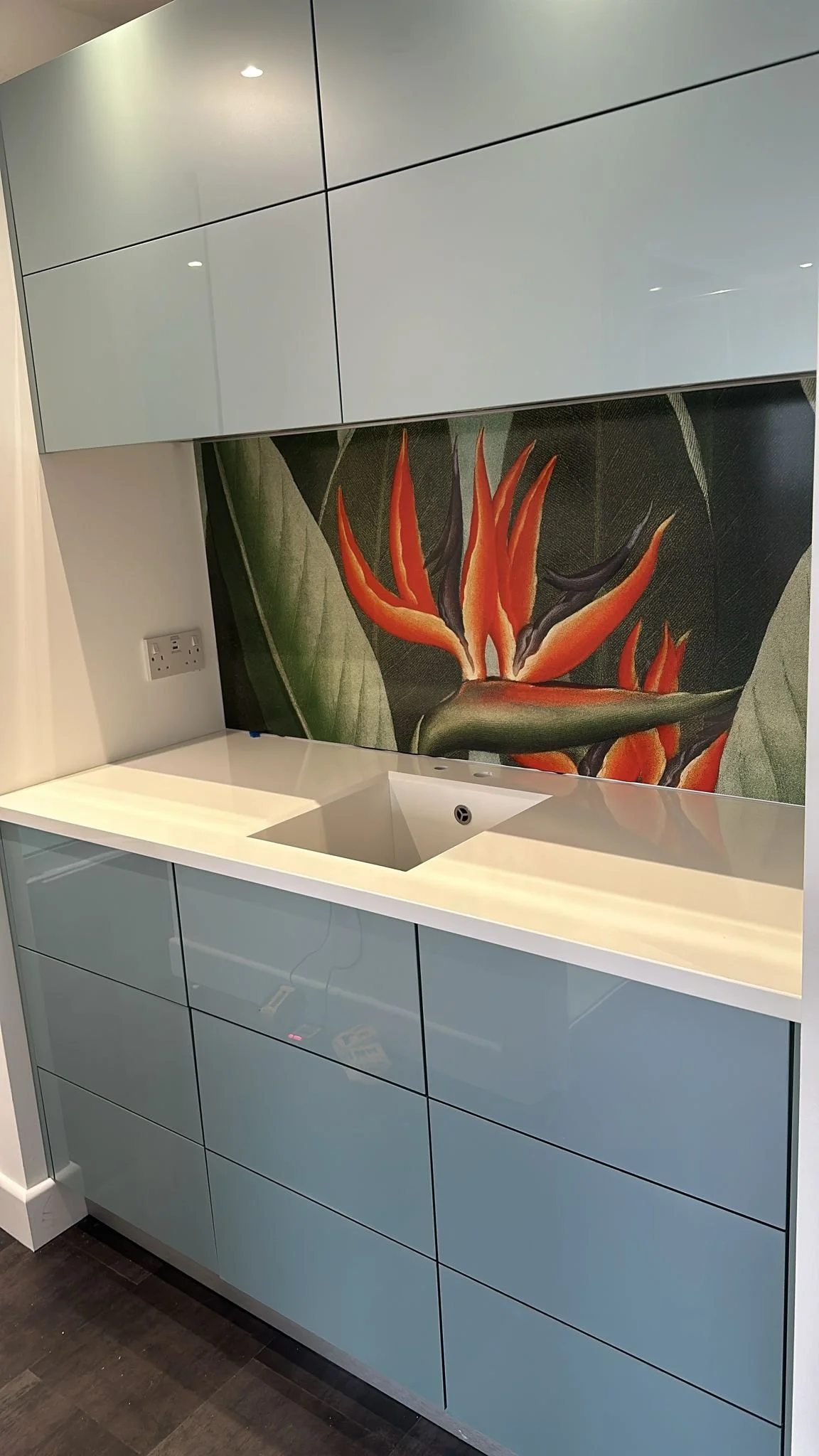 The Queen botanical printed, seamless kitchen splashback in a modern integrated kitchen. Grey cupboards and white Corian sink unit.