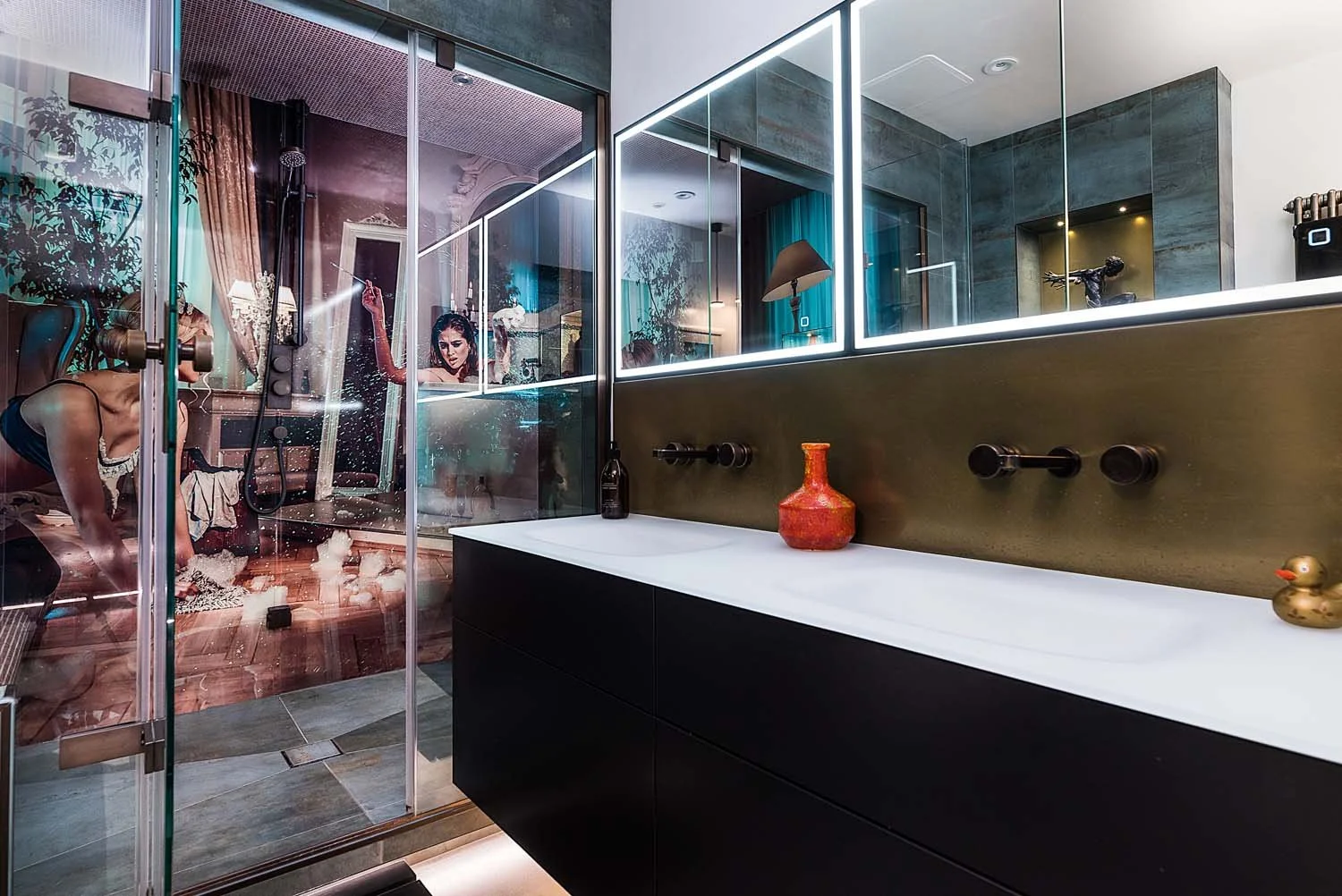 Modern bathroom interior with illuminated mirror above a long, sleek vanity unit. Integrated steam room shower area with sexy French maid image on the shower walls.