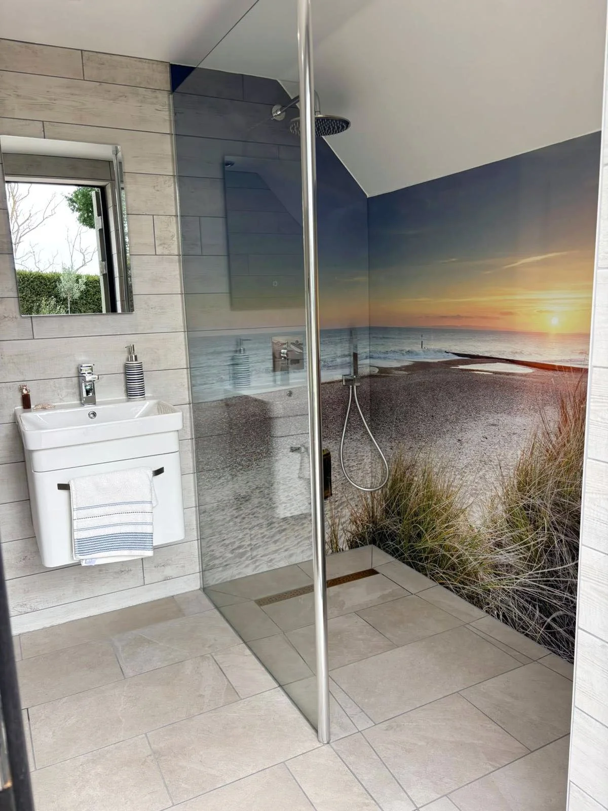 Modern bathroom walk in shower with tiled shower floor, sunset image shower panels and single glass shower panel. Shower panels follow sloping ceiling profile.