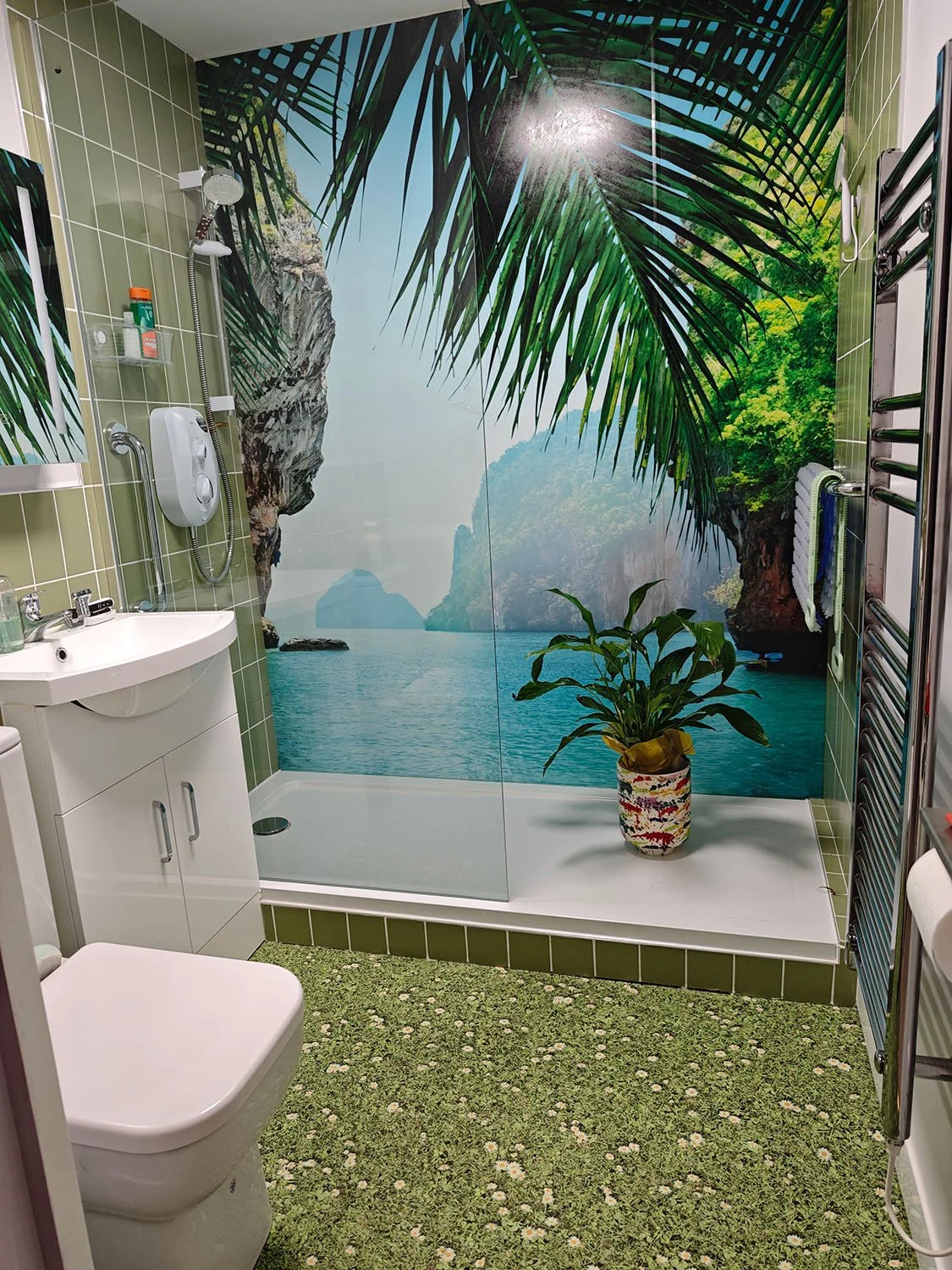 Customer installation photo in bathroom with green colour theme to floor and tiling. Feature shower wall panel of tropical island bay with blue water and palm tree