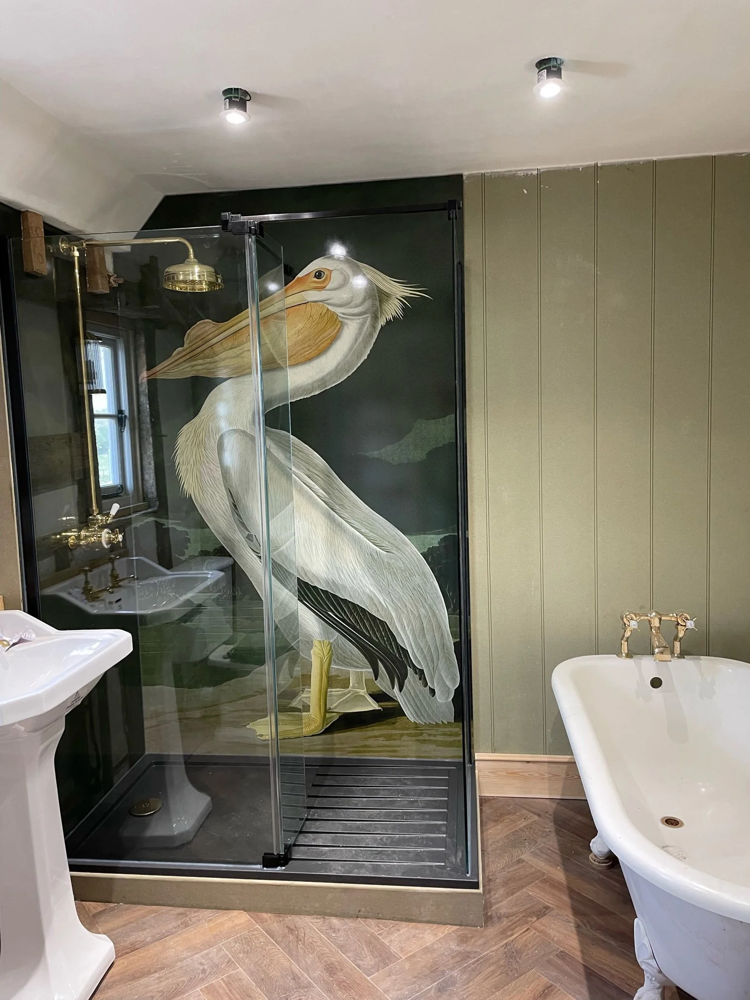 Audubon American White Pelican art print shower panel fitted in a corner shower in a period home bathroom. Traditional green themed bathroom with wooden floor, wooden panelled walls.