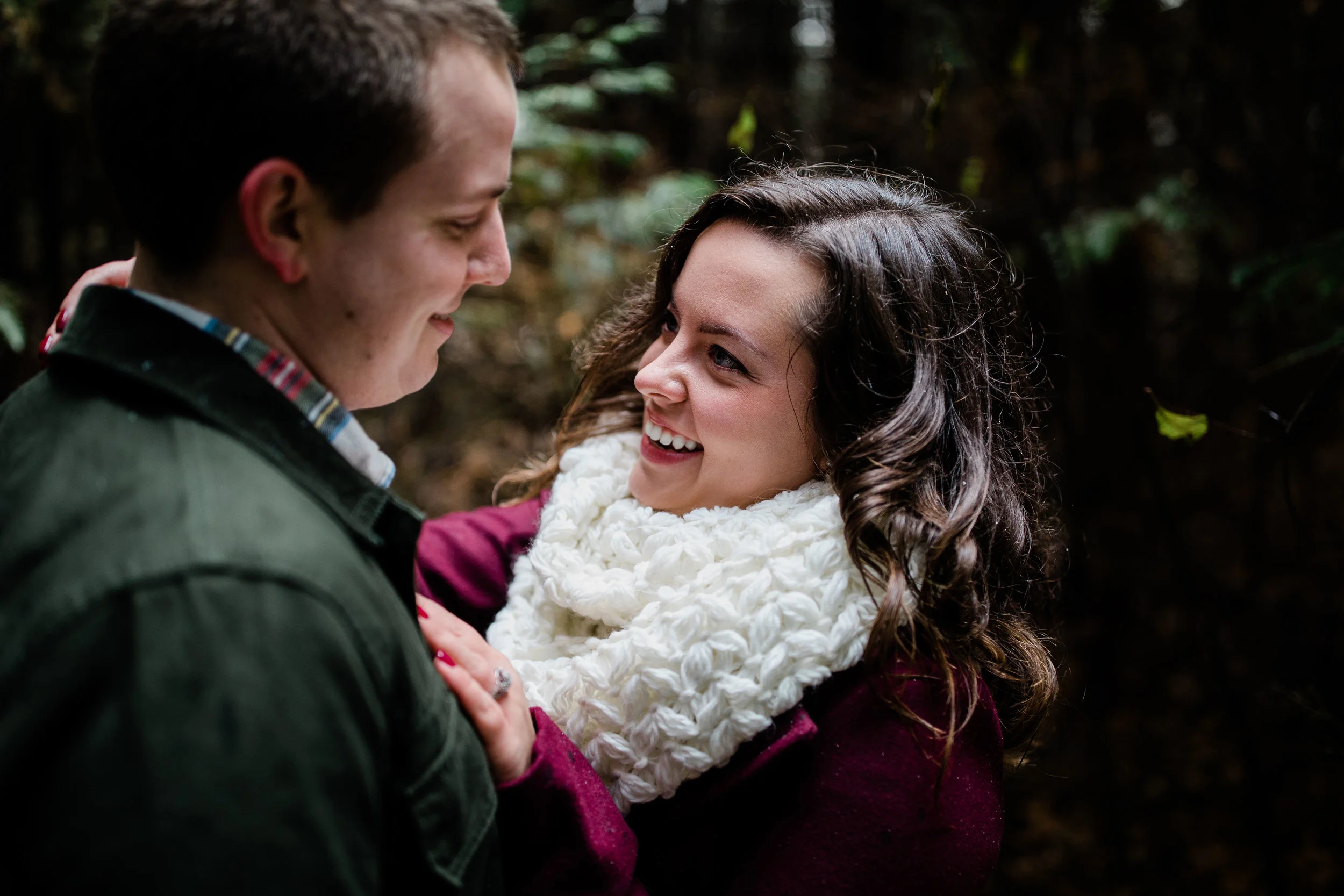 Couple holds each other close and smiles in the woods.